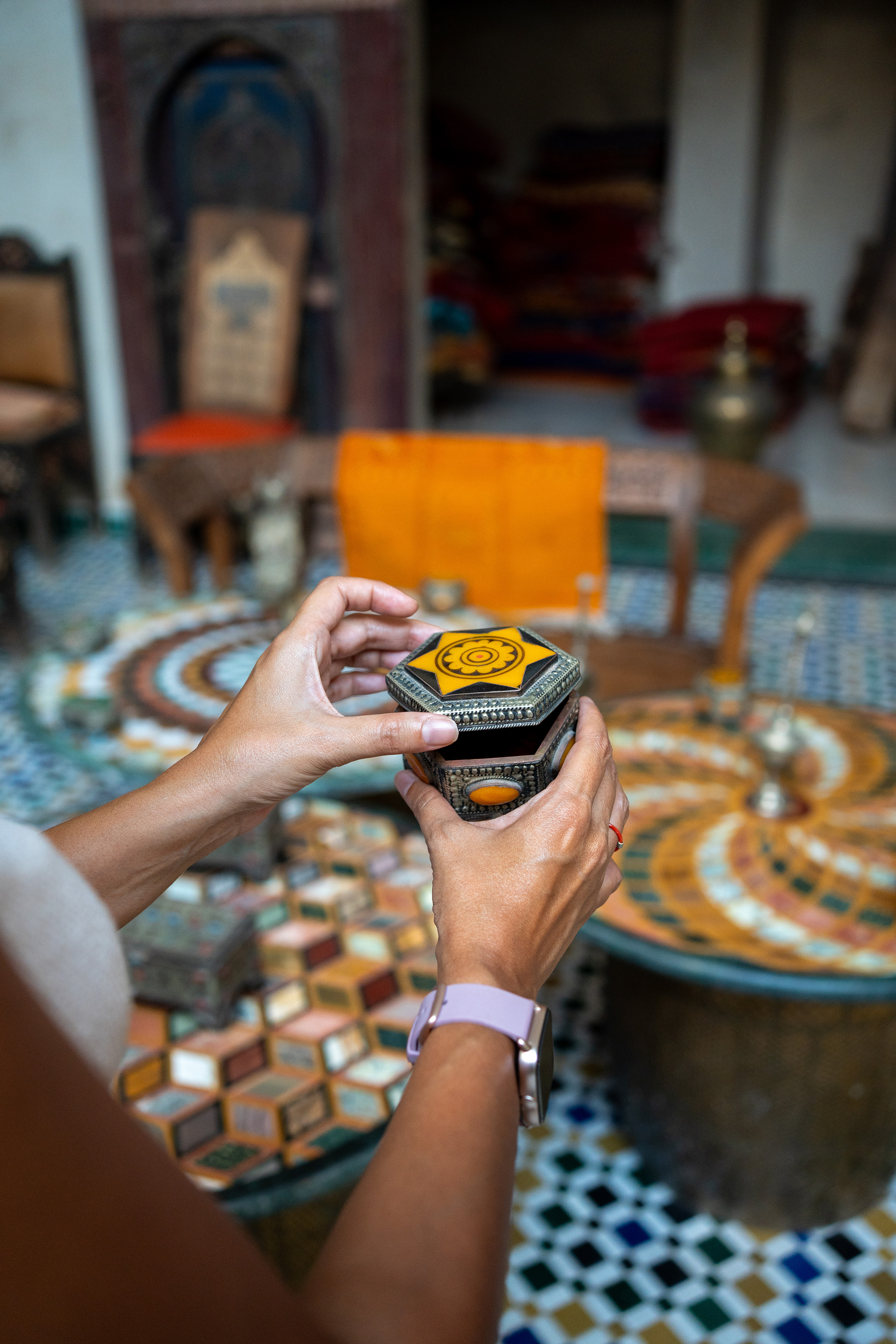 Hands opening ornate Moroccan hexagonal jewelry box with yellow geometric patterns.