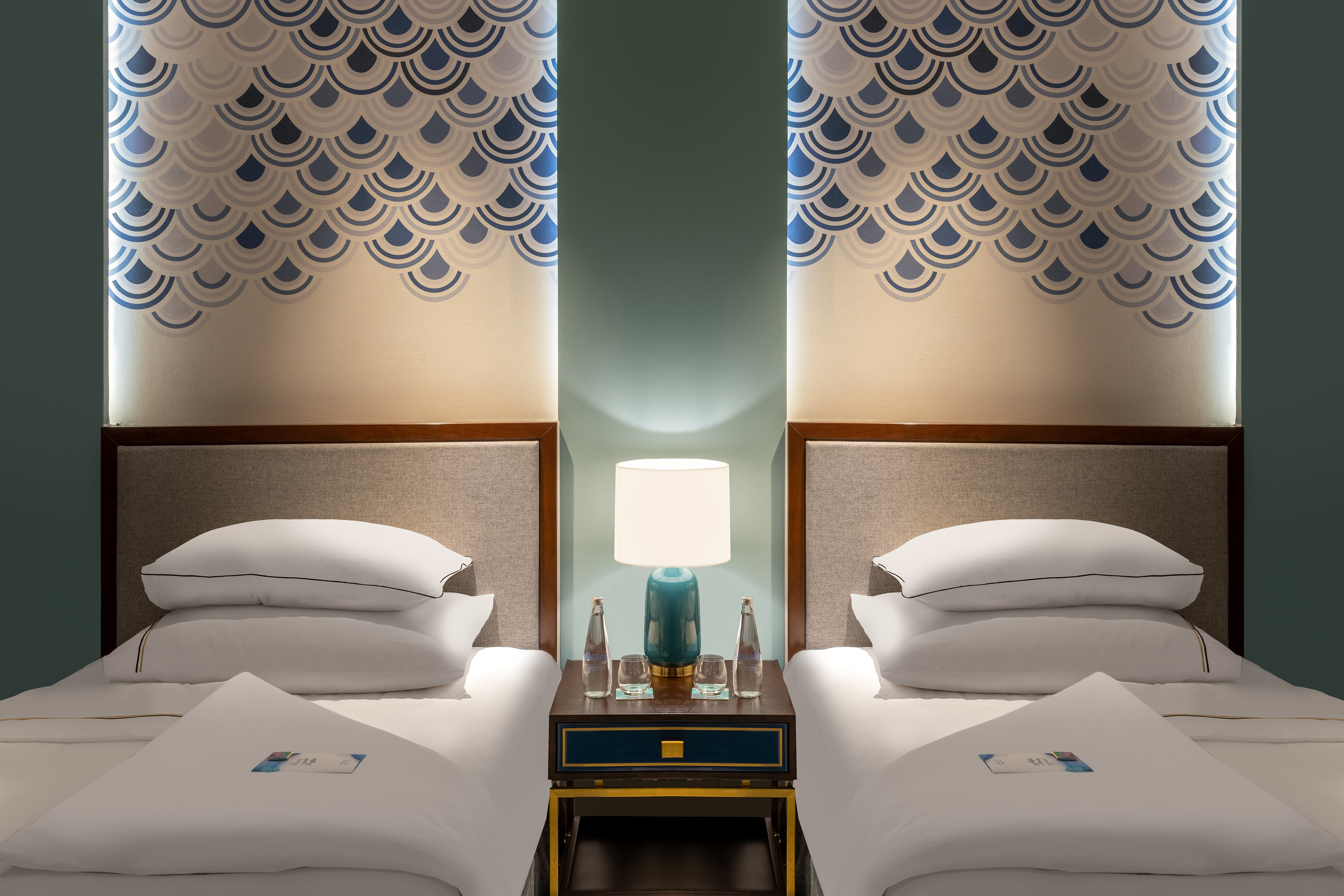 Twin guest room with white beds, nightstand, lamp, and blue scallop wall art.