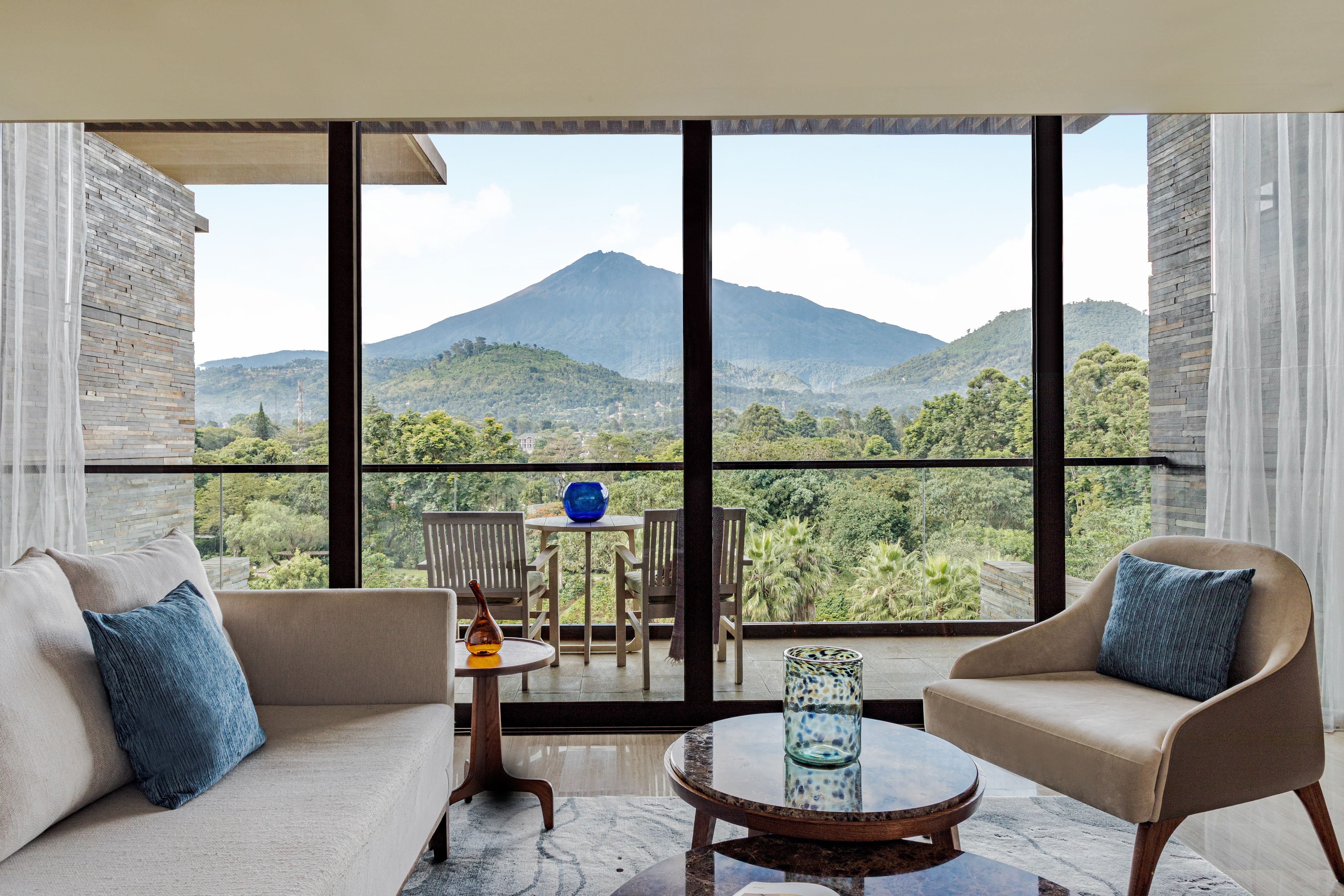 Modern living room with mountain view, balcony, and lush green landscape.