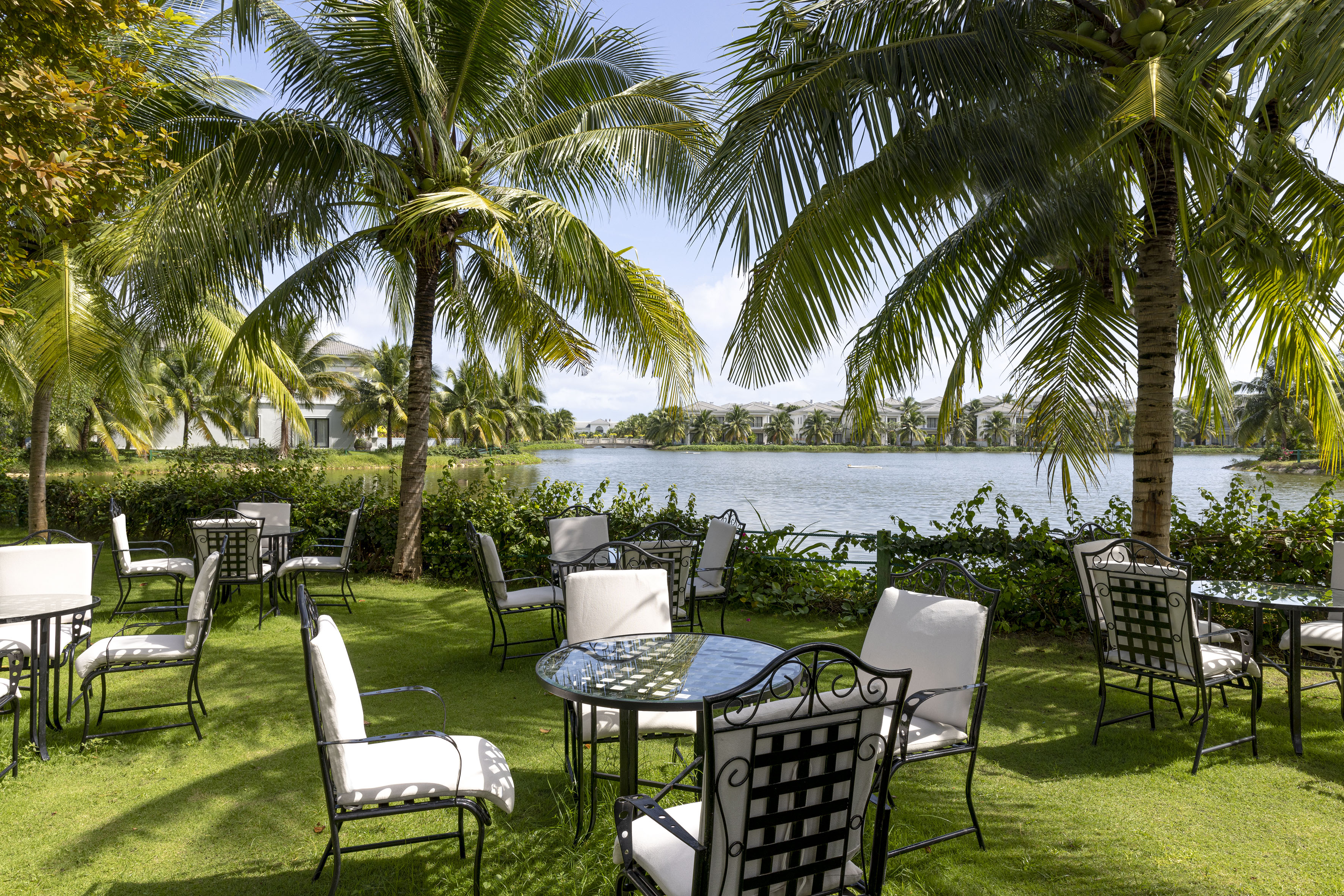 Tropical resort patio with tables, palm trees, and lake view.