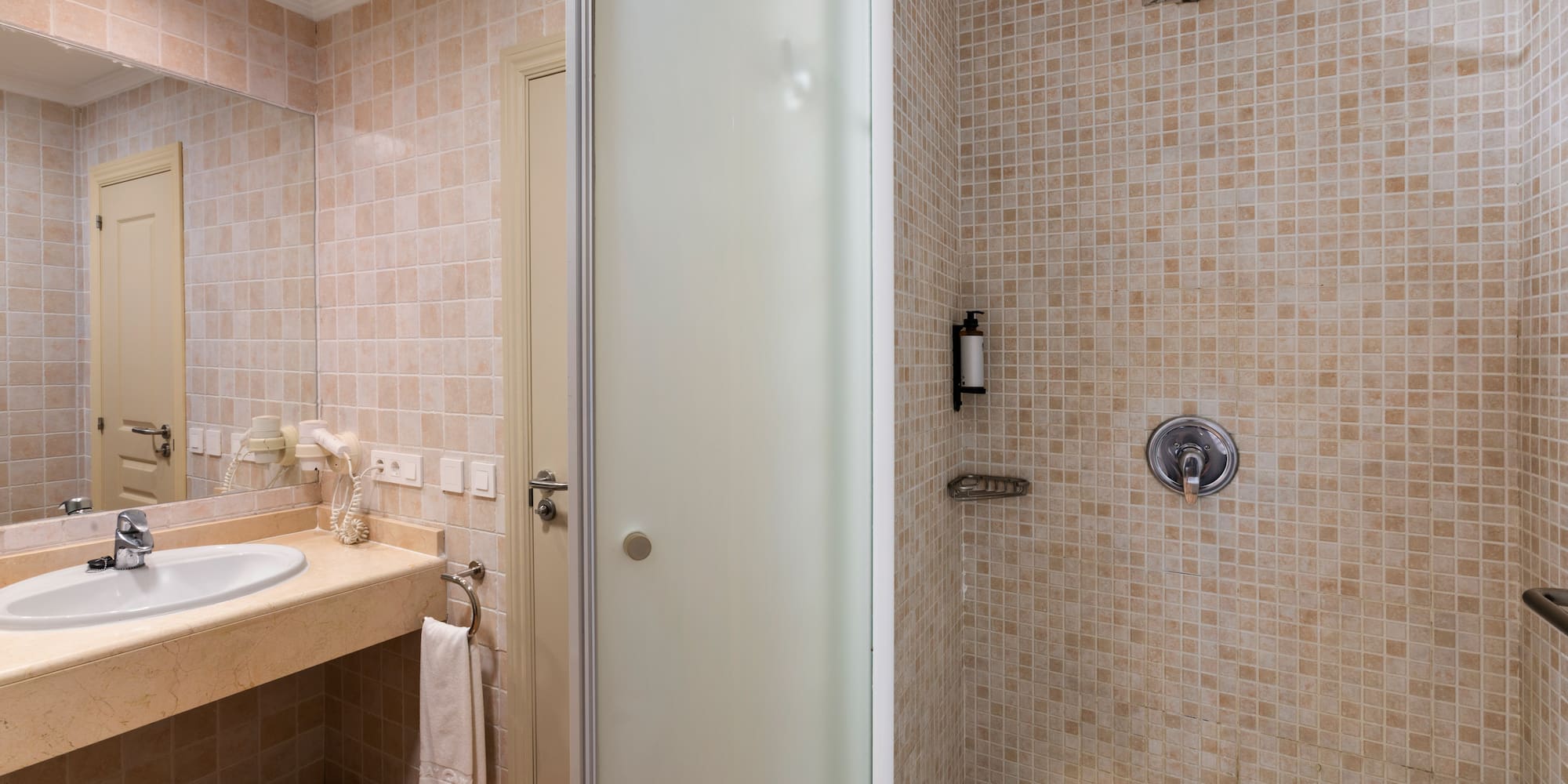 Modern hotel bathroom with vanity sink, mirror, and tiled shower with rainfall head.