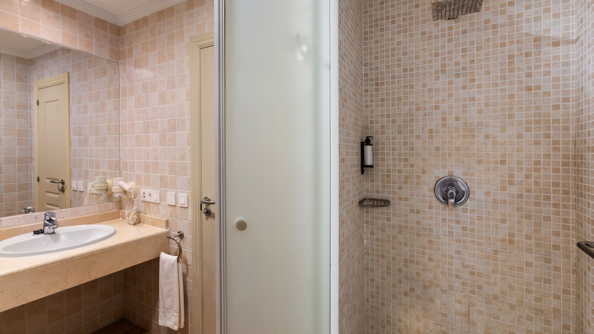 Beige tiled bathroom with vanity sink, mirror, and glass shower cabin.