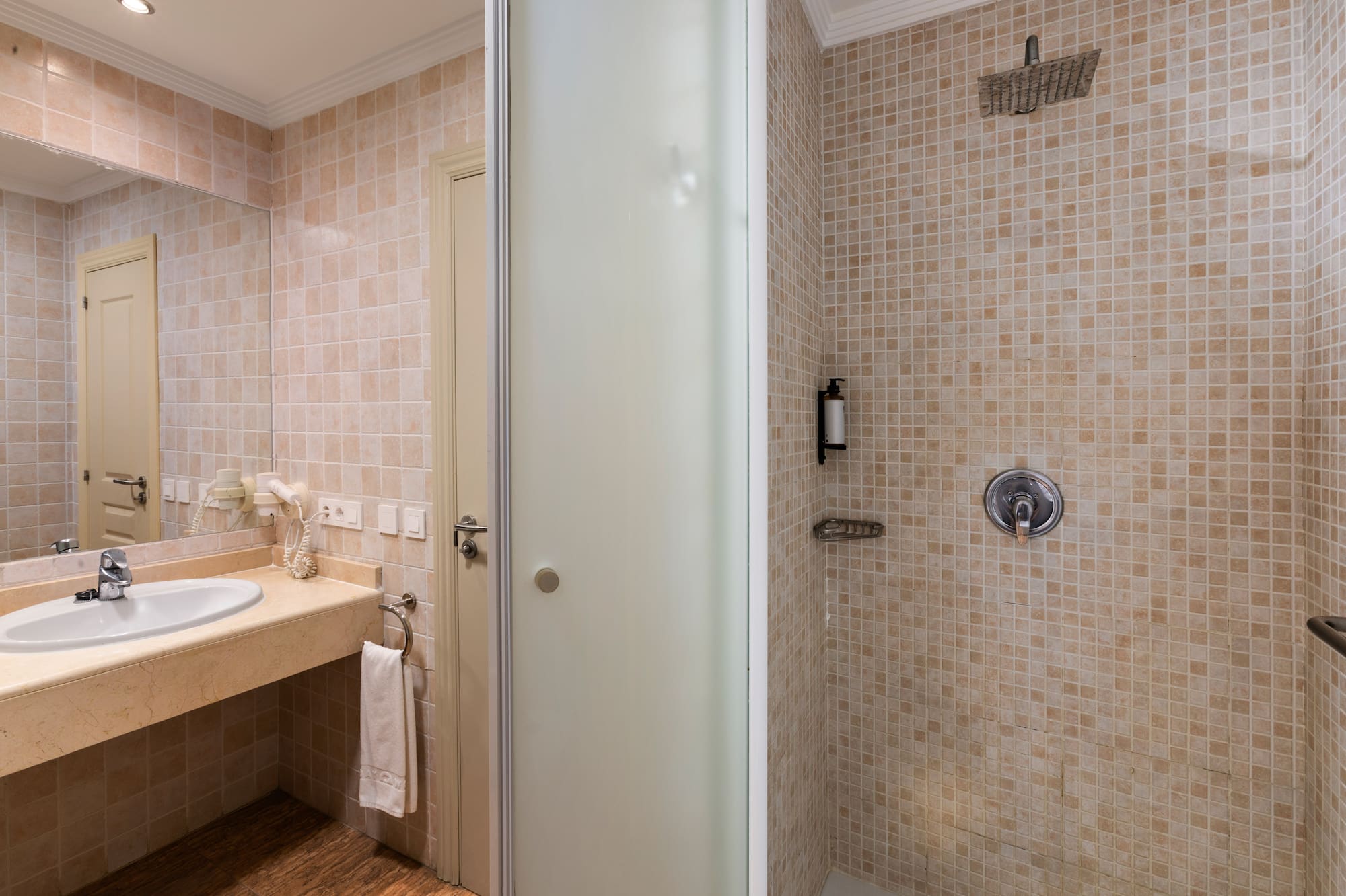 Beige tiled bathroom with vanity sink, mirror, and glass shower cabin.