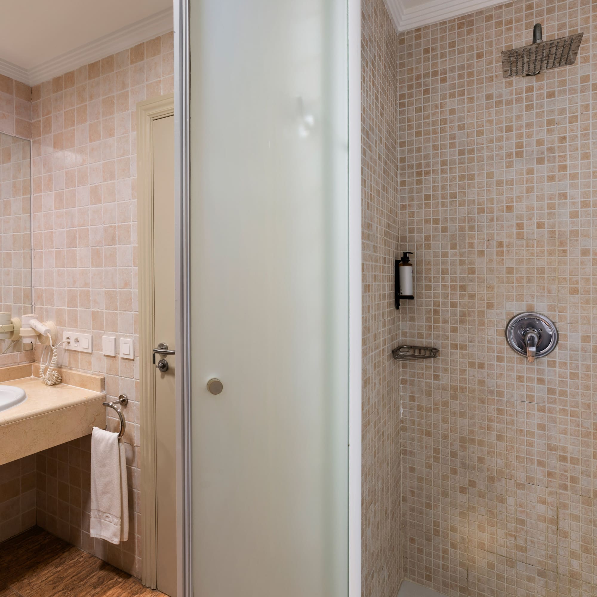 Modern hotel bathroom with vanity sink, mirror, and tiled shower with rainfall head.