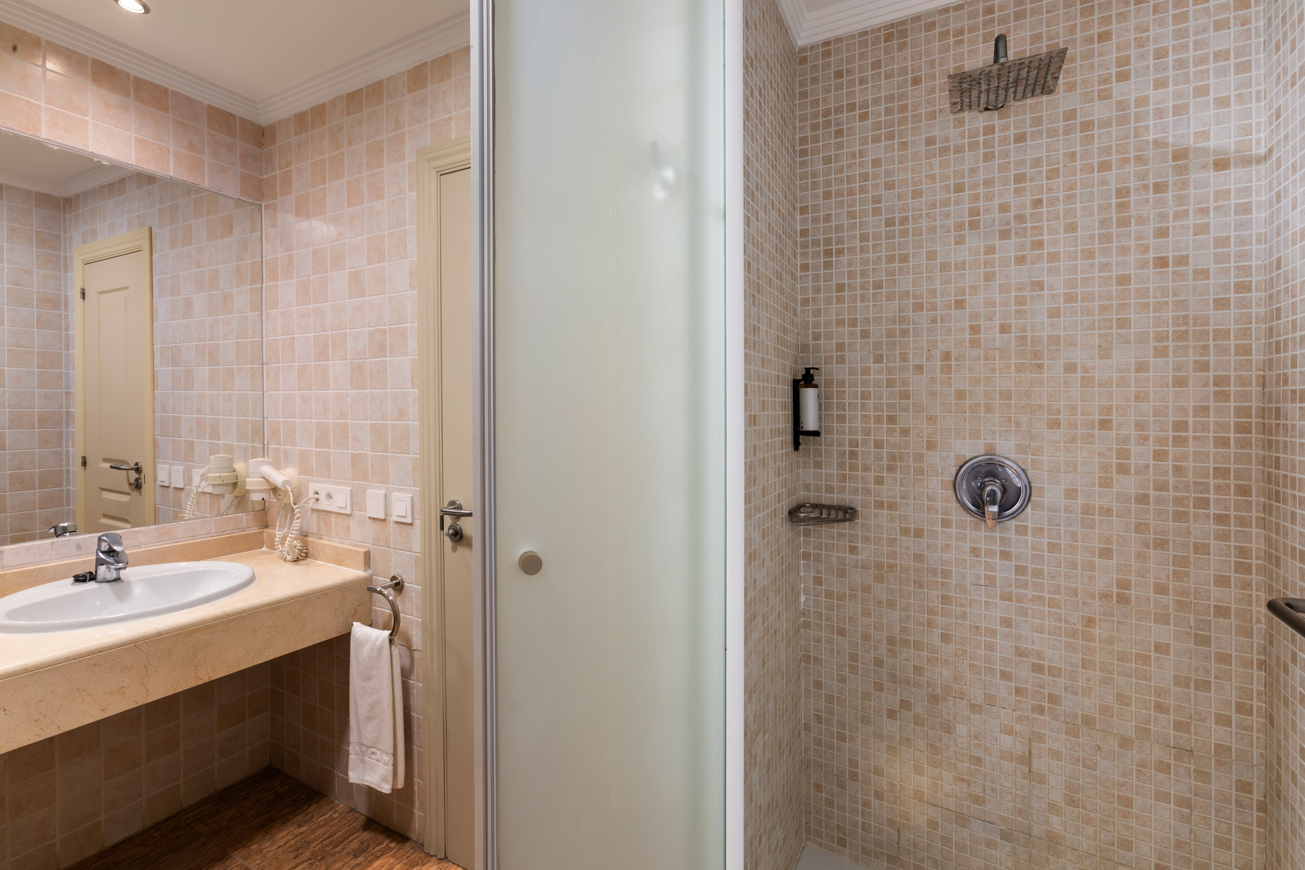 Beige tiled bathroom with vanity sink, mirror, and glass shower cabin.