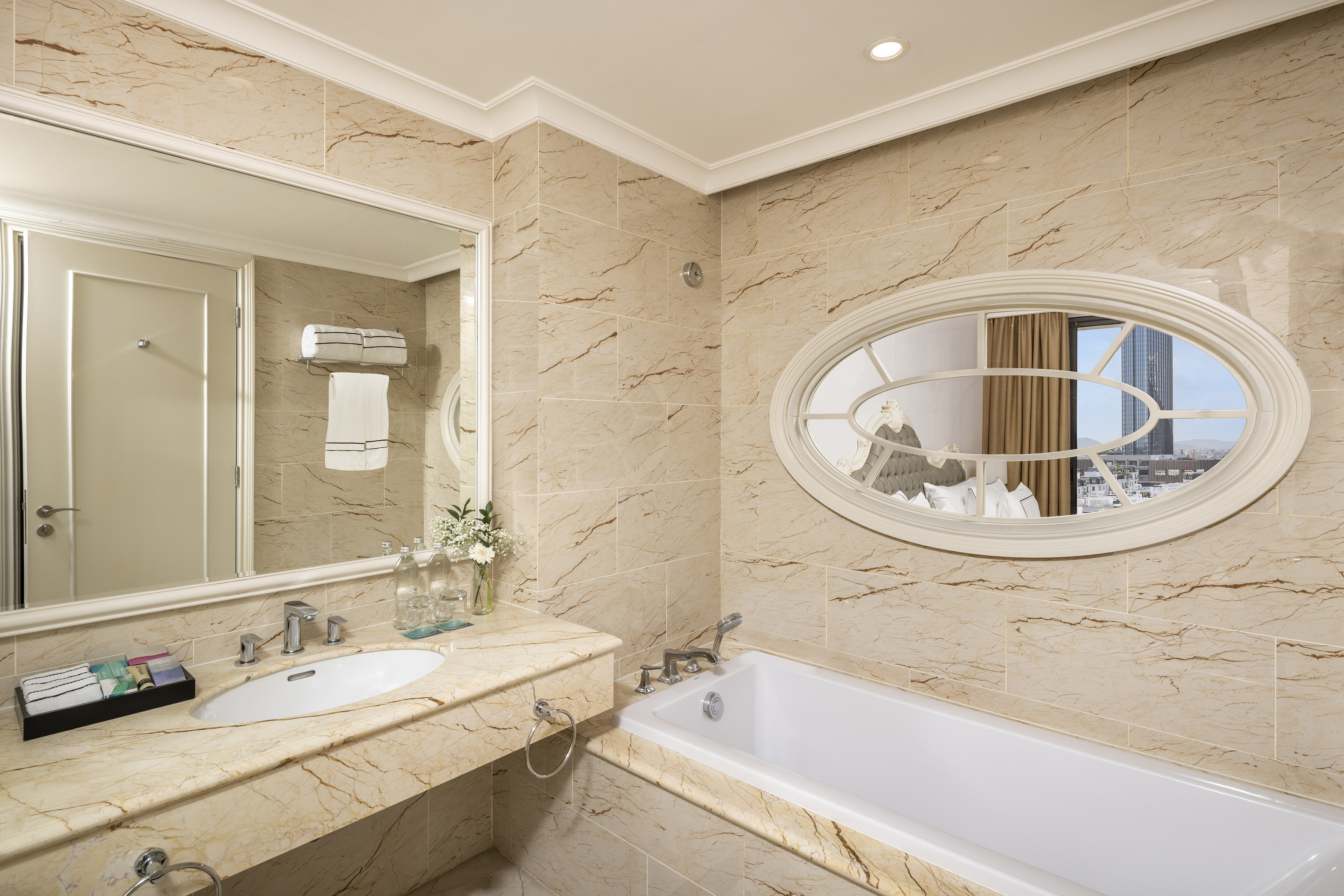 Luxury hotel bathroom with marble walls, vanity, bathtub, and oval window.