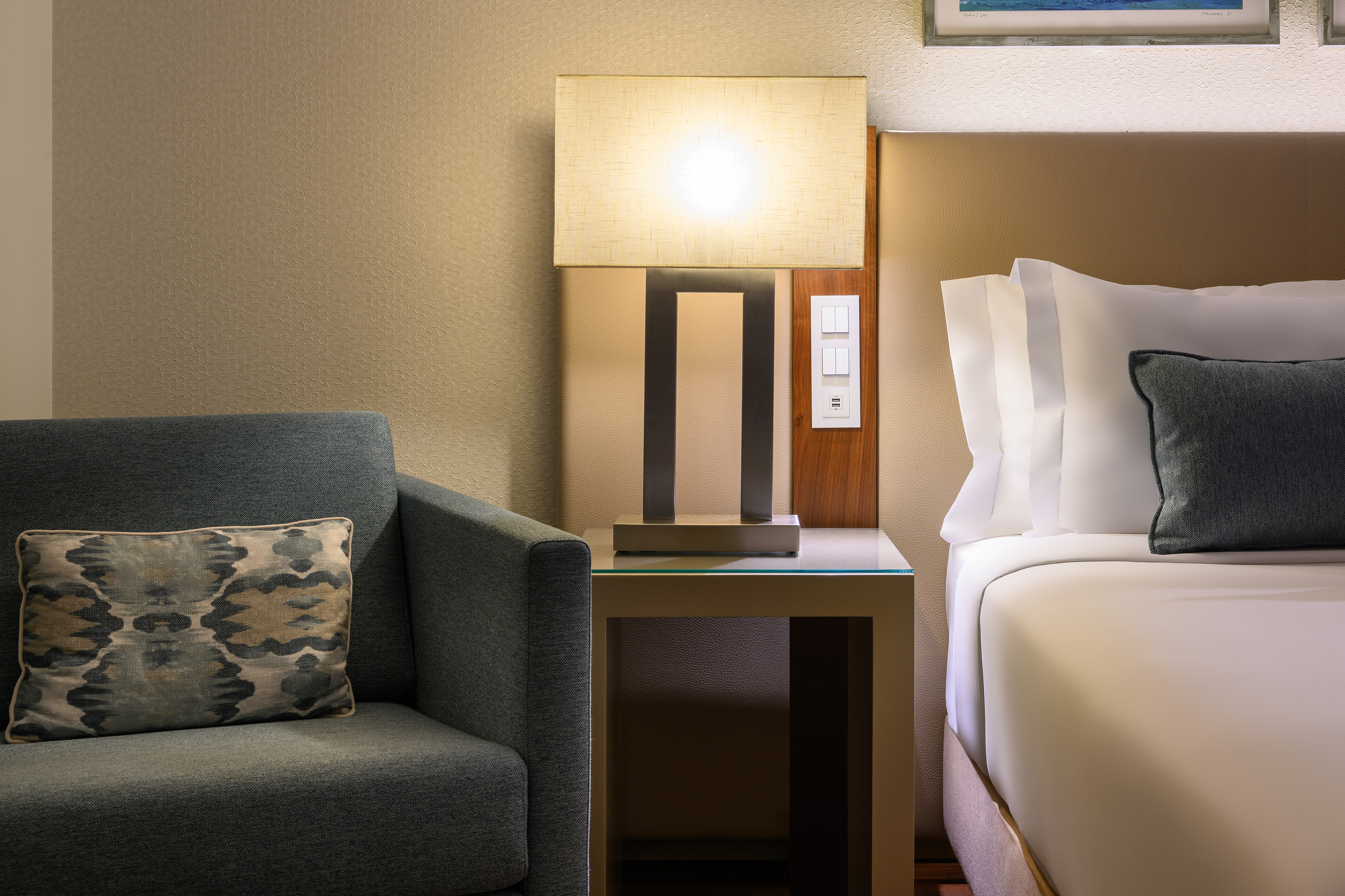 Cozy hotel room with bed, armchair, and illuminated bedside lamp.