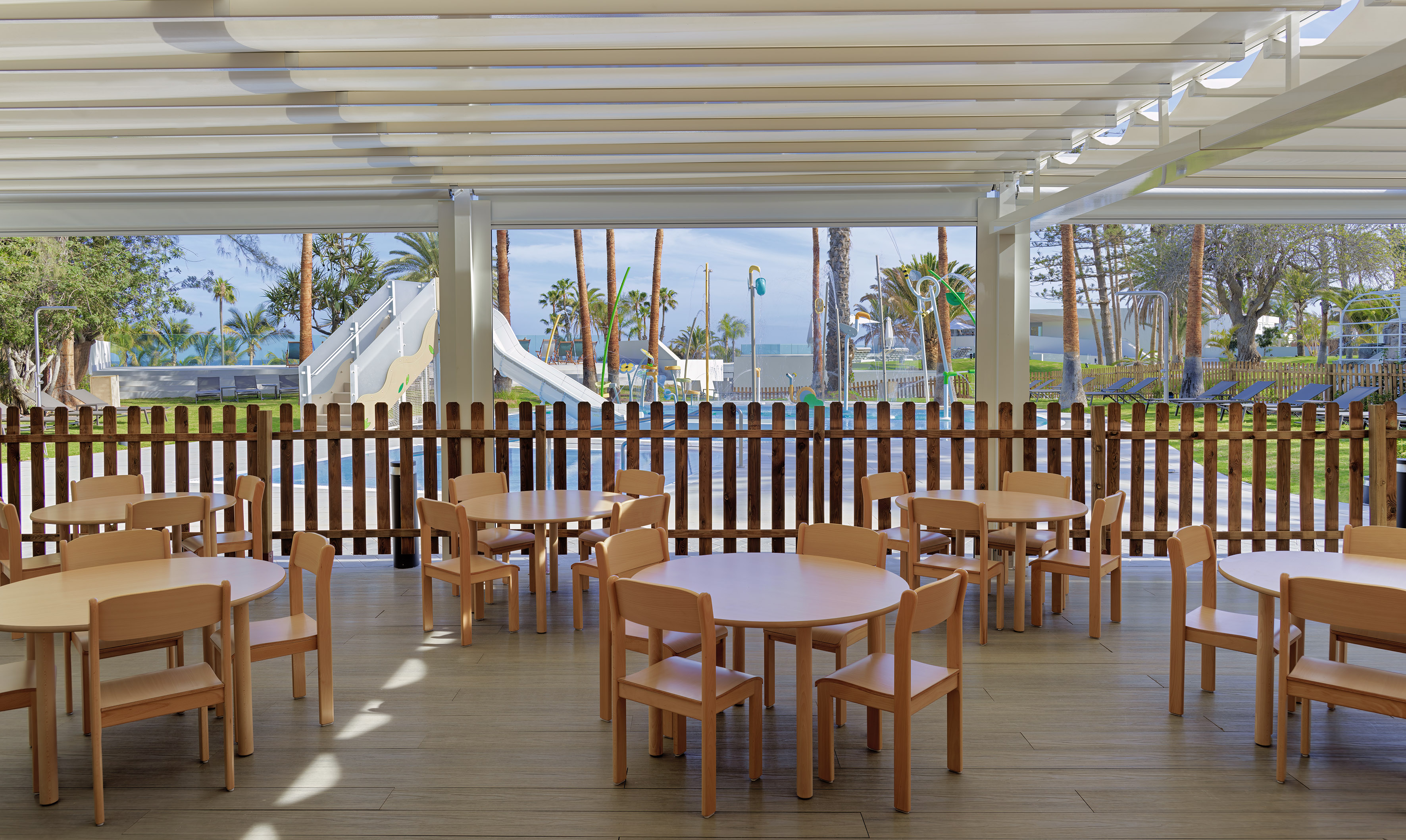 Kids' outdoor dining area by pool, with water slides and palm trees.