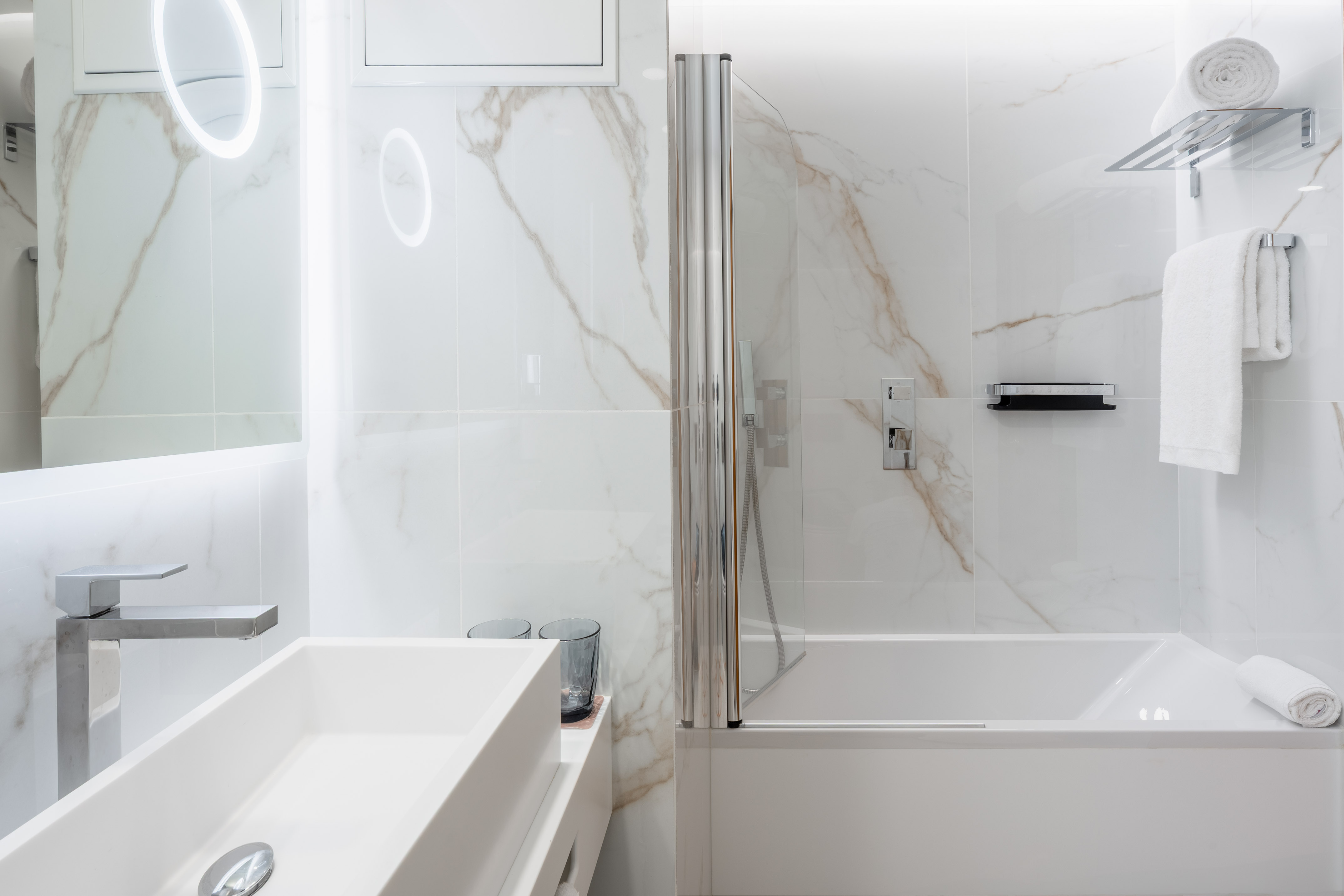 Modern white marble bathroom with sink, illuminated mirror, and tub-shower.