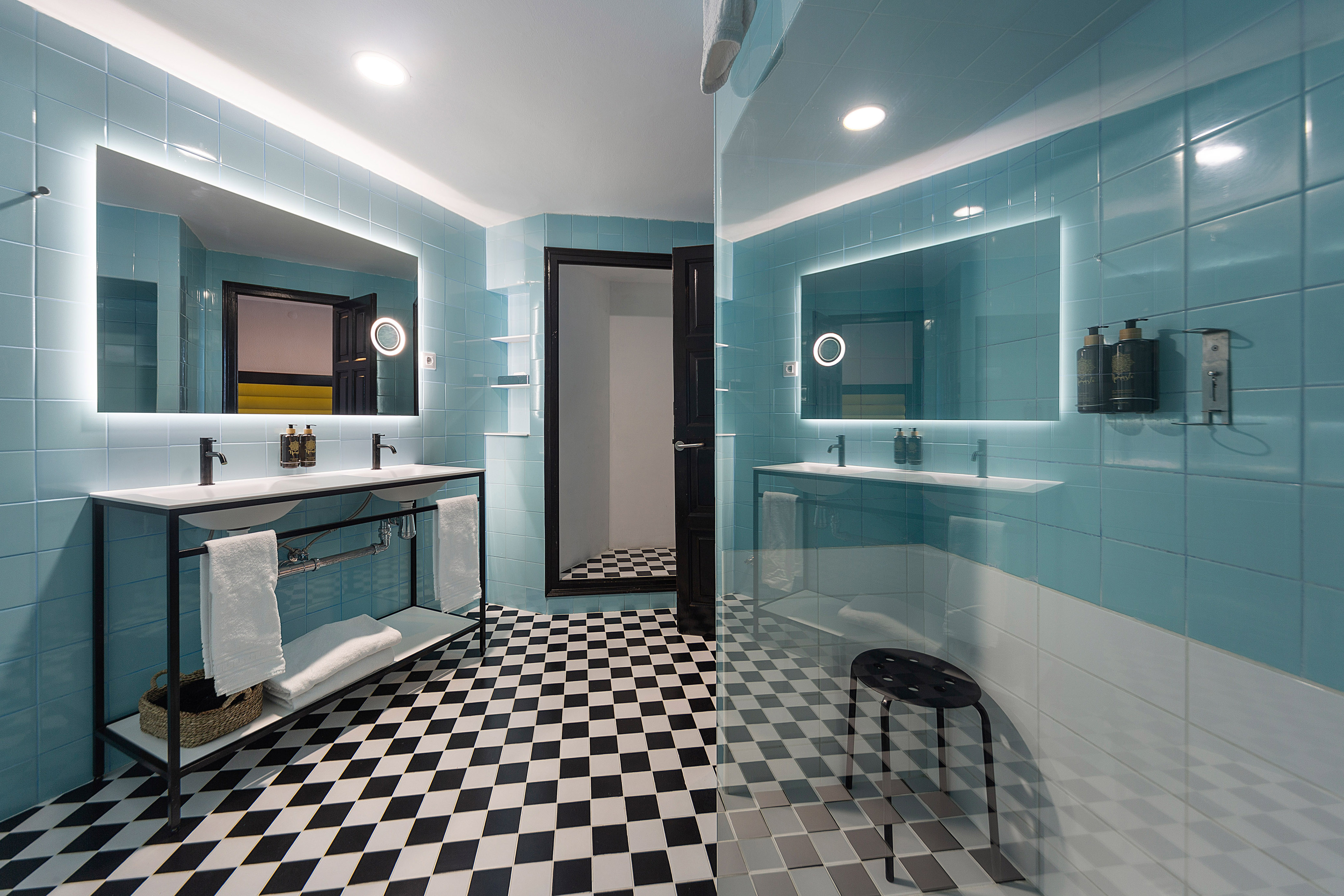 Hotel bathroom with light blue tiles, checkered floor, modern dual vanity.