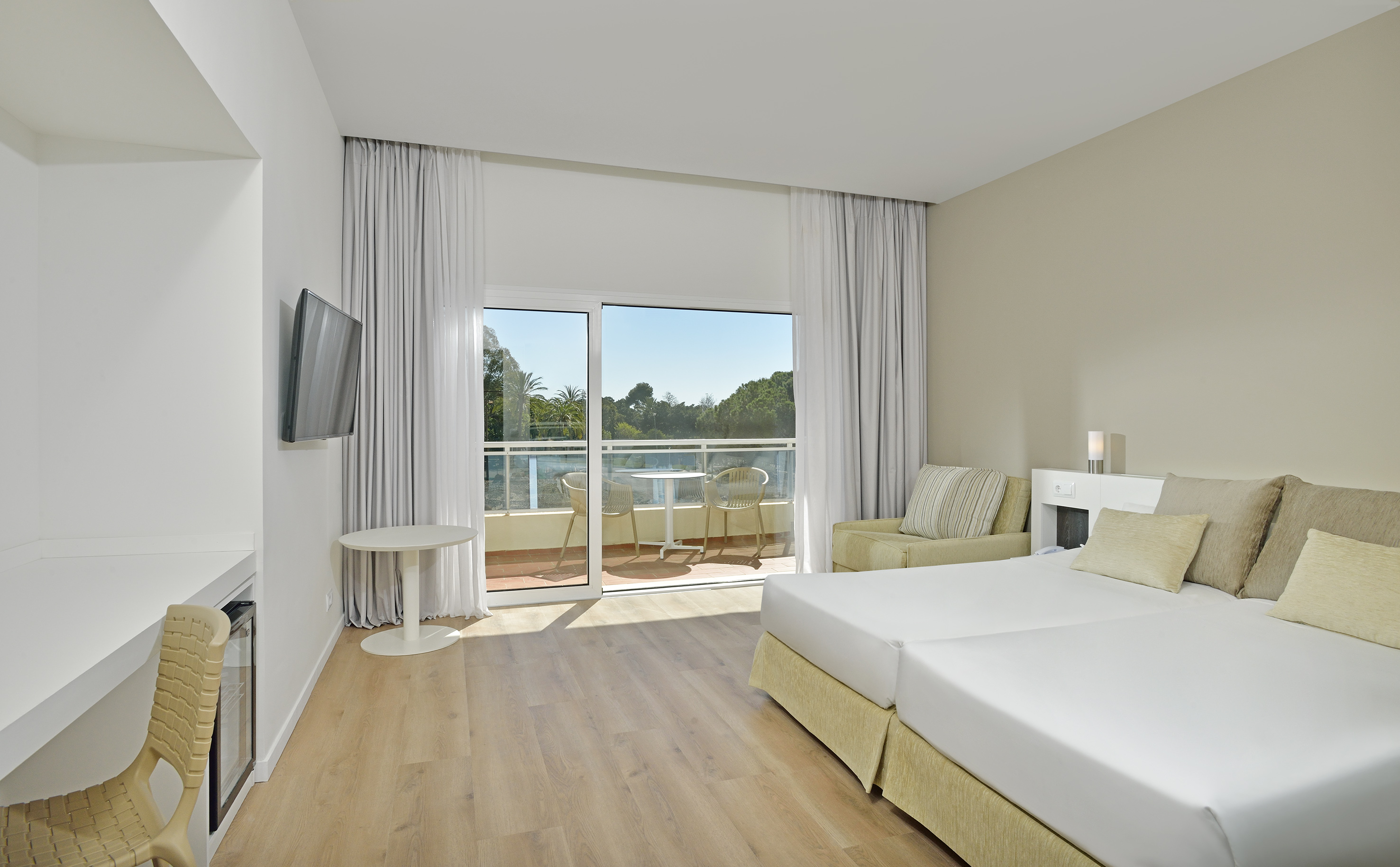 Modern hotel room with twin beds, balcony, desk, and resort view.