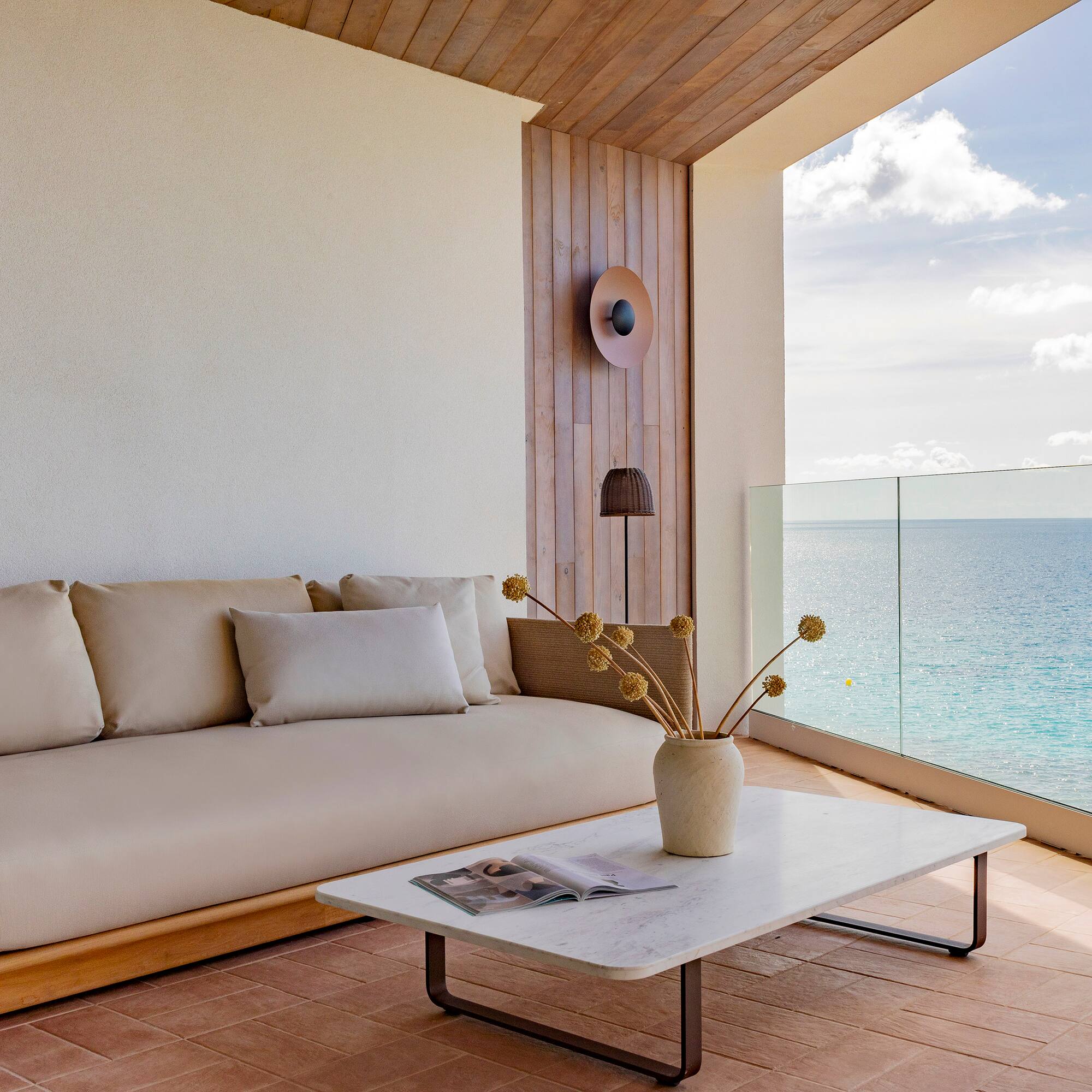 a couch and coffee table on a deck with a view of the ocean