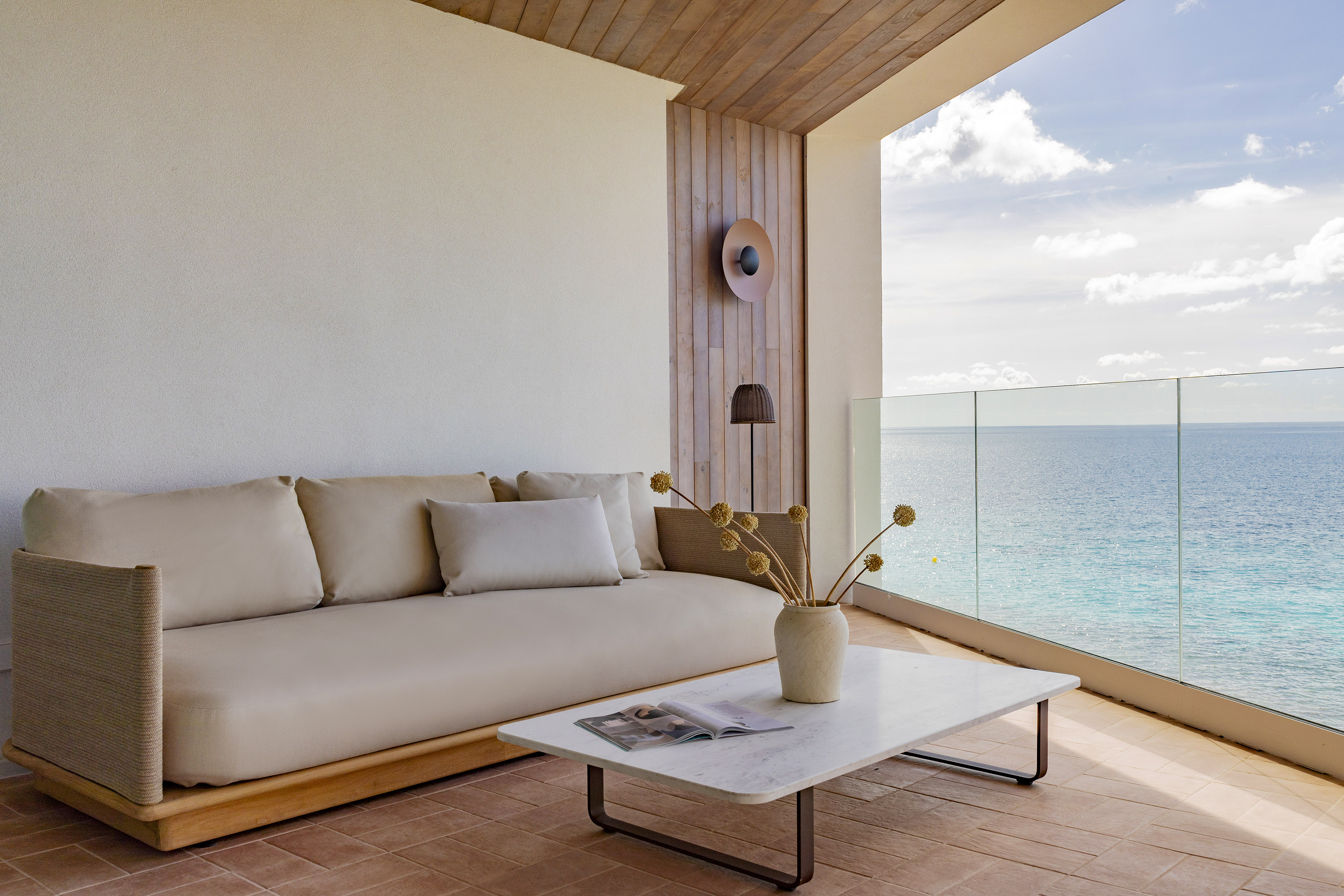 Modern balcony with neutral sofa, marble table, and expansive ocean view.