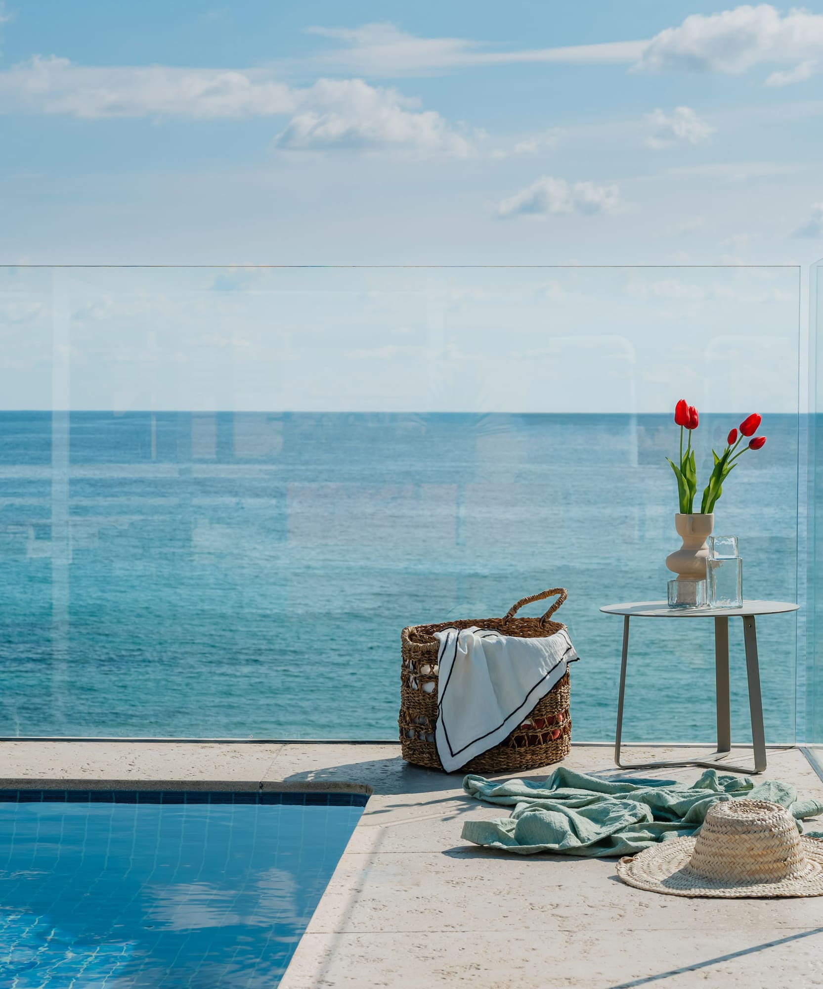 Piscina infinita con vista al mar, terraza de lujo con cesta, mesa y tulipanes.