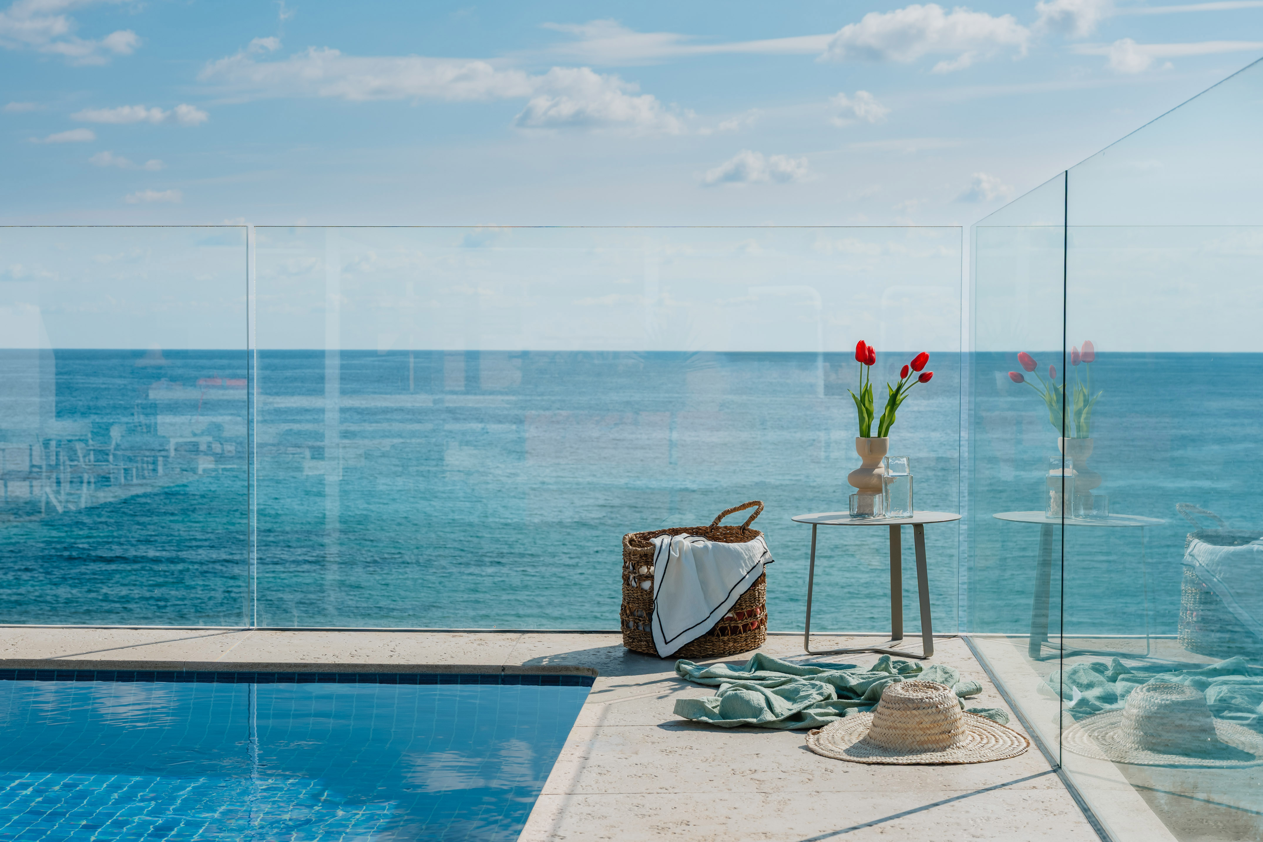 Piscina infinita con vista al mar, terraza de lujo con cesta, mesa y tulipanes.