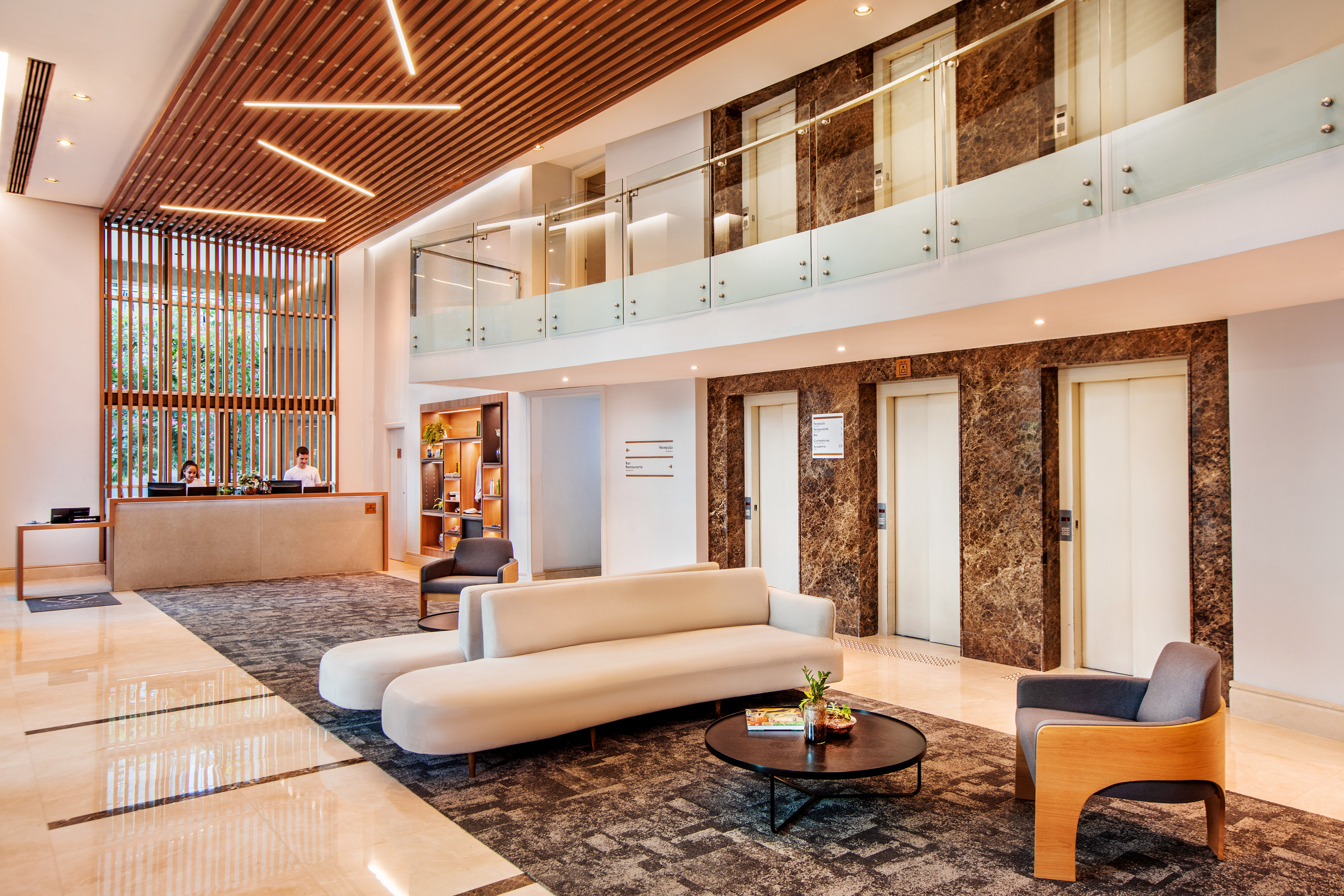 Contemporary hotel lobby with reception desk, seating area, and elevators.