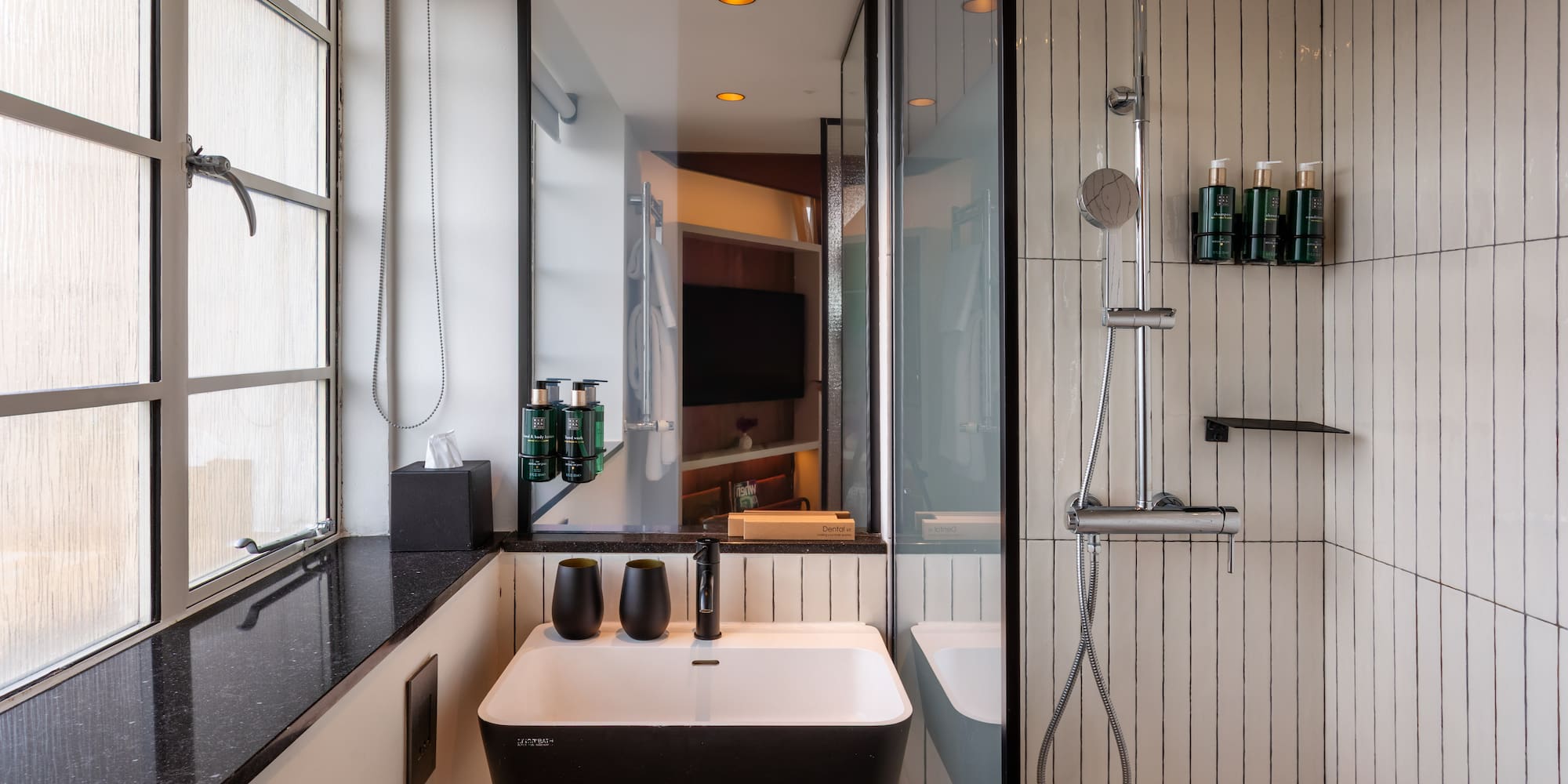 Modern hotel bathroom with black and white vanity, sink, and walk-in shower.