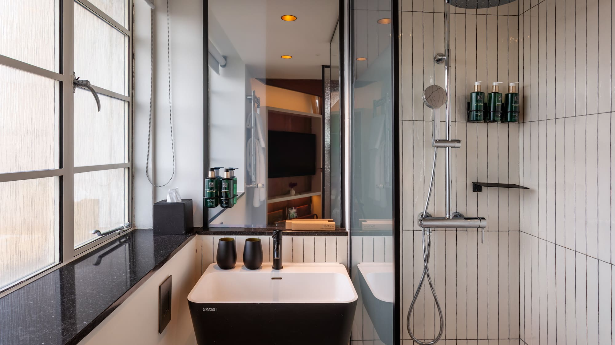 Modern hotel bathroom with black and white vanity, sink, and walk-in shower.