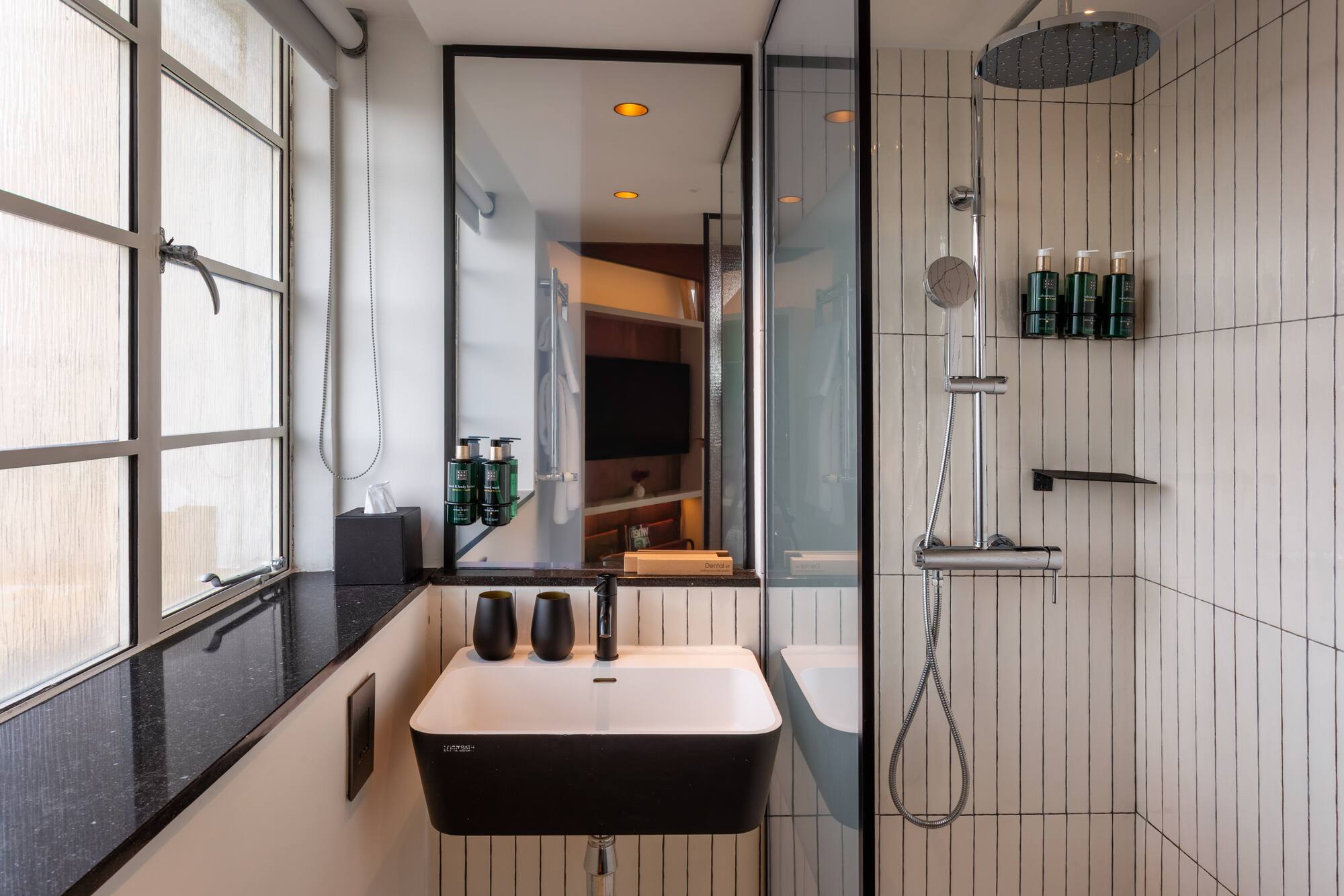 Modern hotel bathroom with black and white vanity, sink, and walk-in shower.