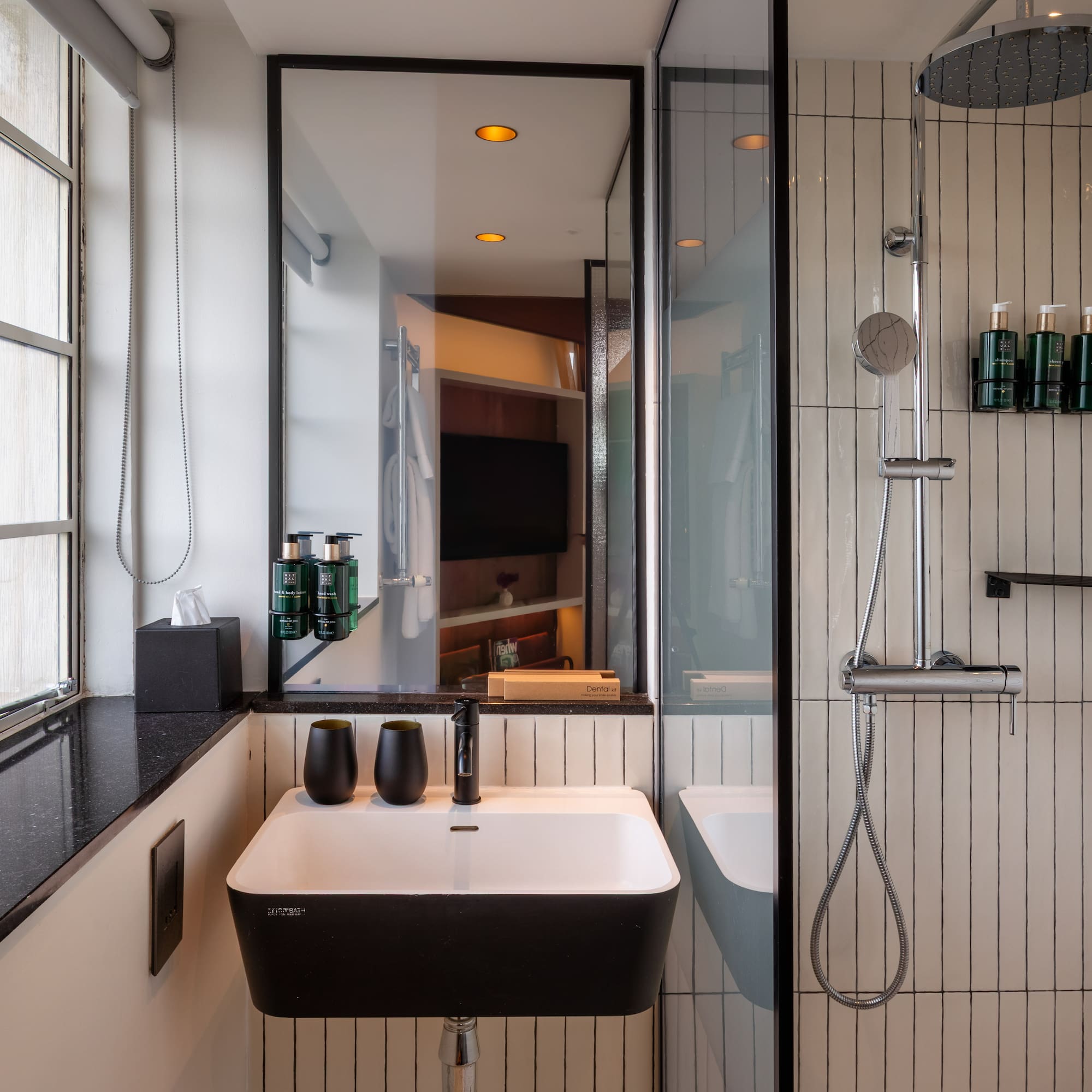 Modern hotel bathroom with black and white vanity, sink, and walk-in shower.