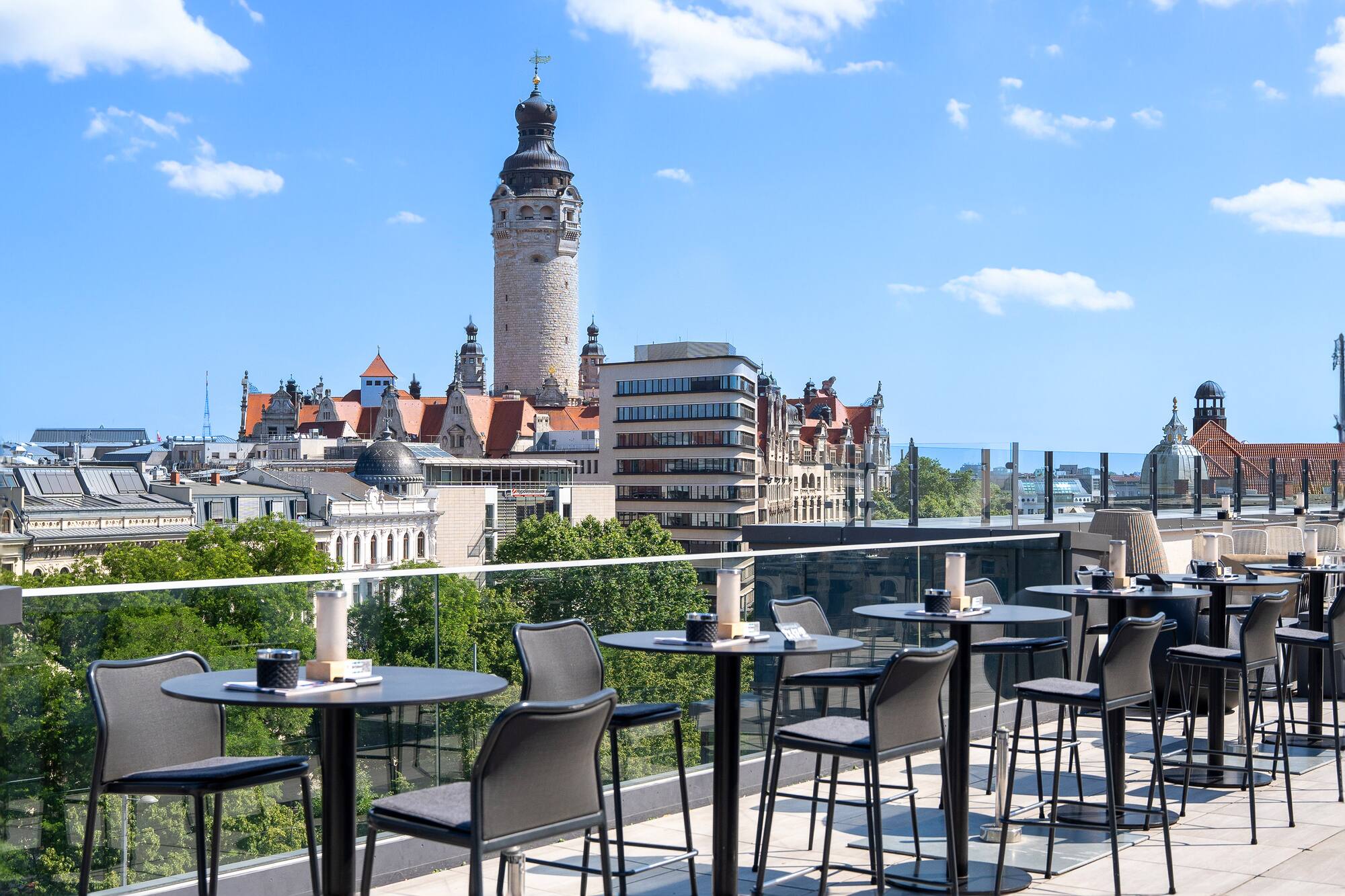 Rooftop bar with Leipzig city view and New Town Hall tower against blue sky.