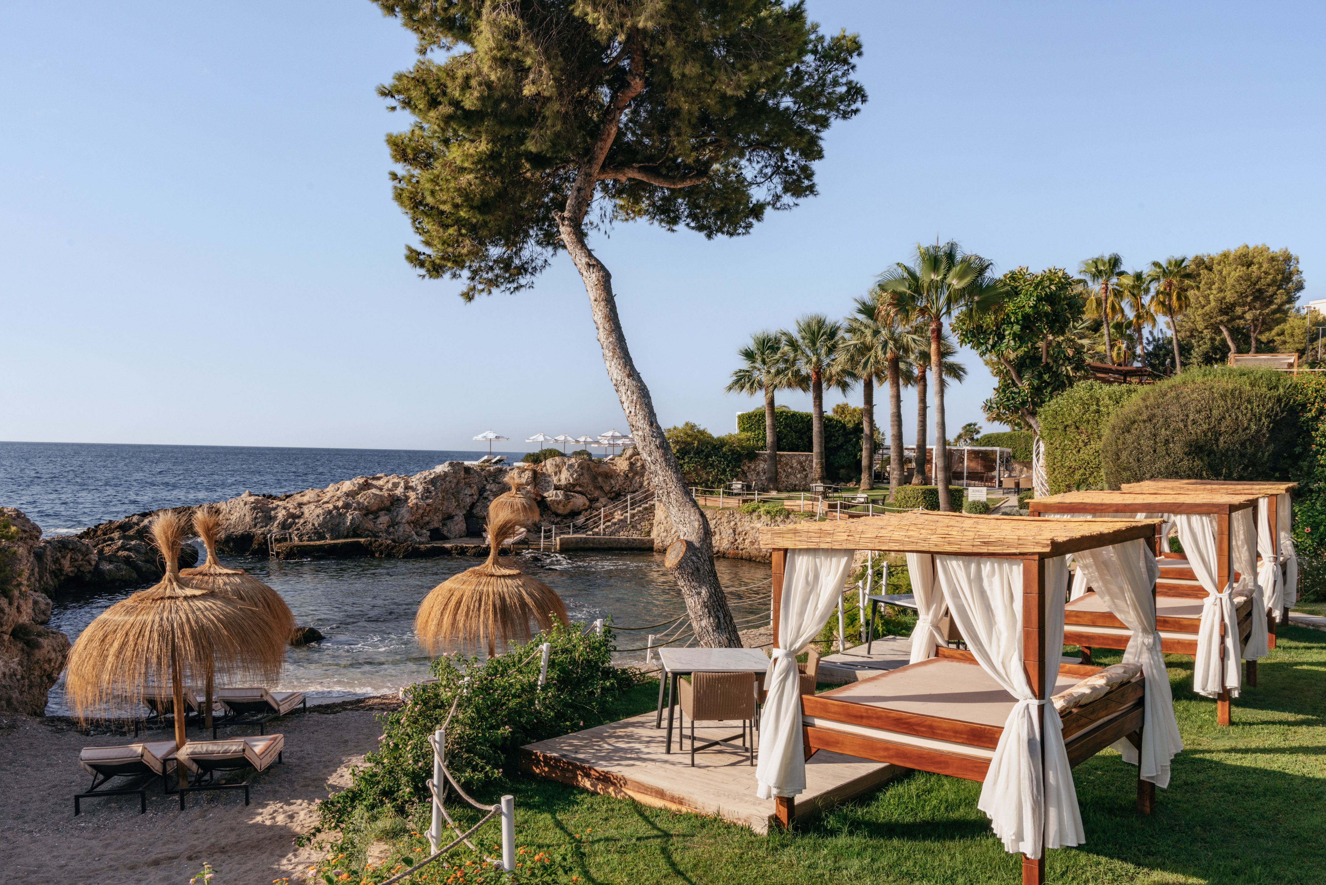 Mediterranean resort with beach cabanas, thatched umbrellas, and palm trees.