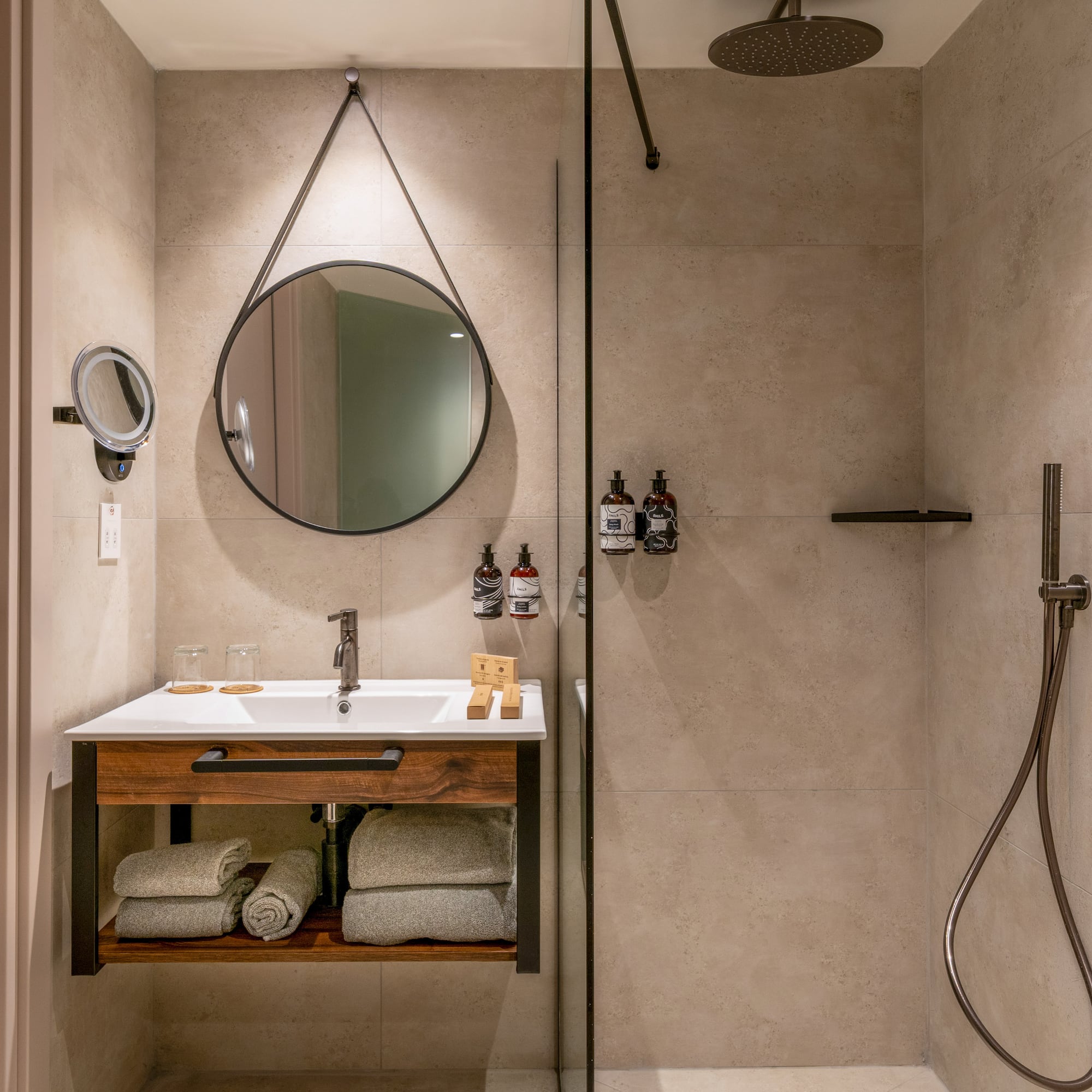 Modern hotel bathroom with wood vanity, round mirror, and walk-in shower.