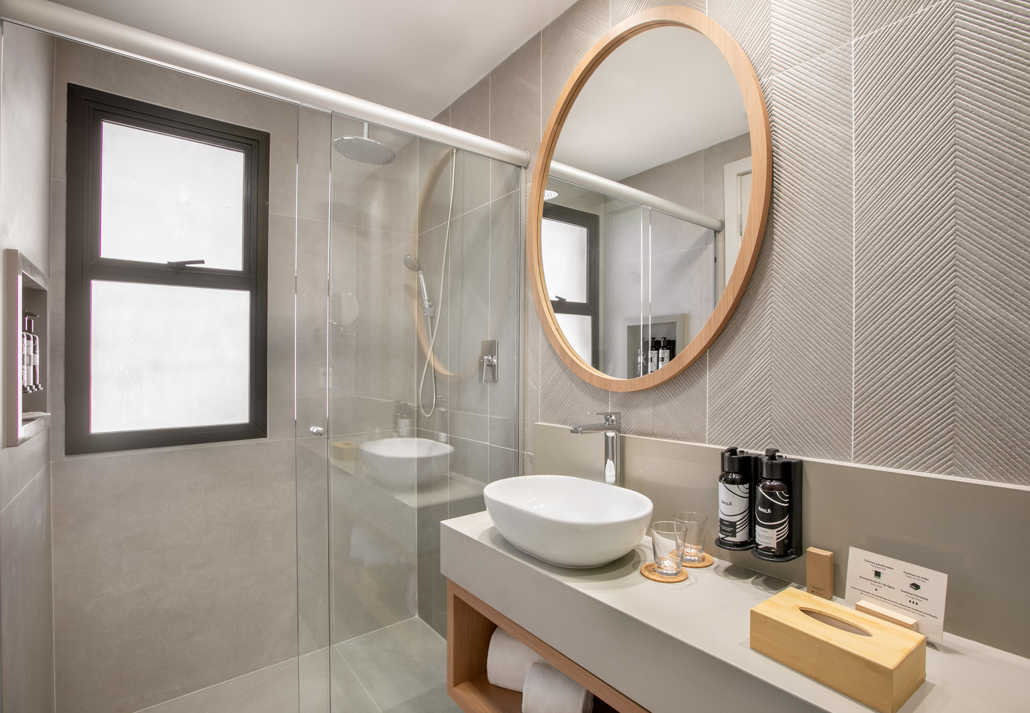 Modern bathroom with glass shower, vessel sink, round mirror, neutral tones.