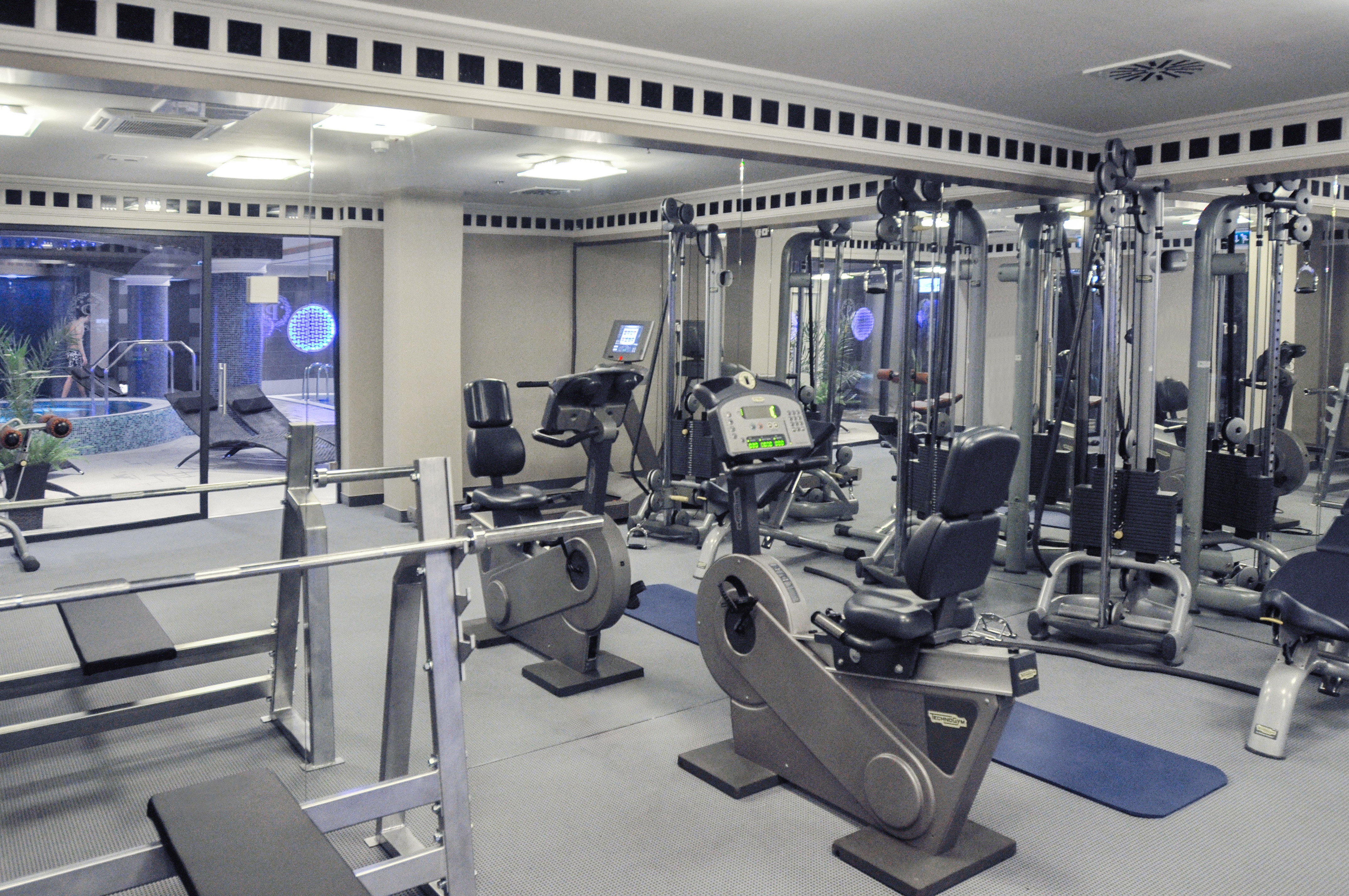Hotel gym with cardio and weight machines, view of indoor pool and jacuzzi.
