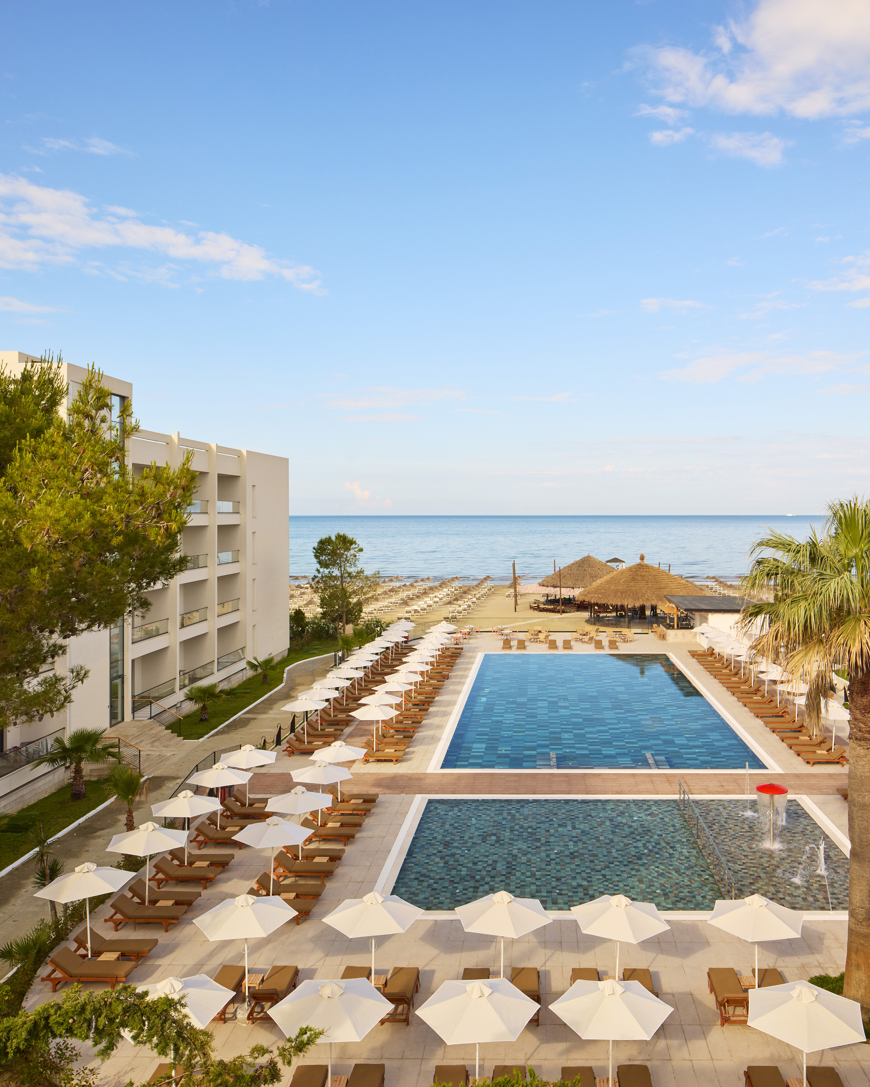 Modern beachfront resort with swimming pools, sunbeds, beach, and ocean.