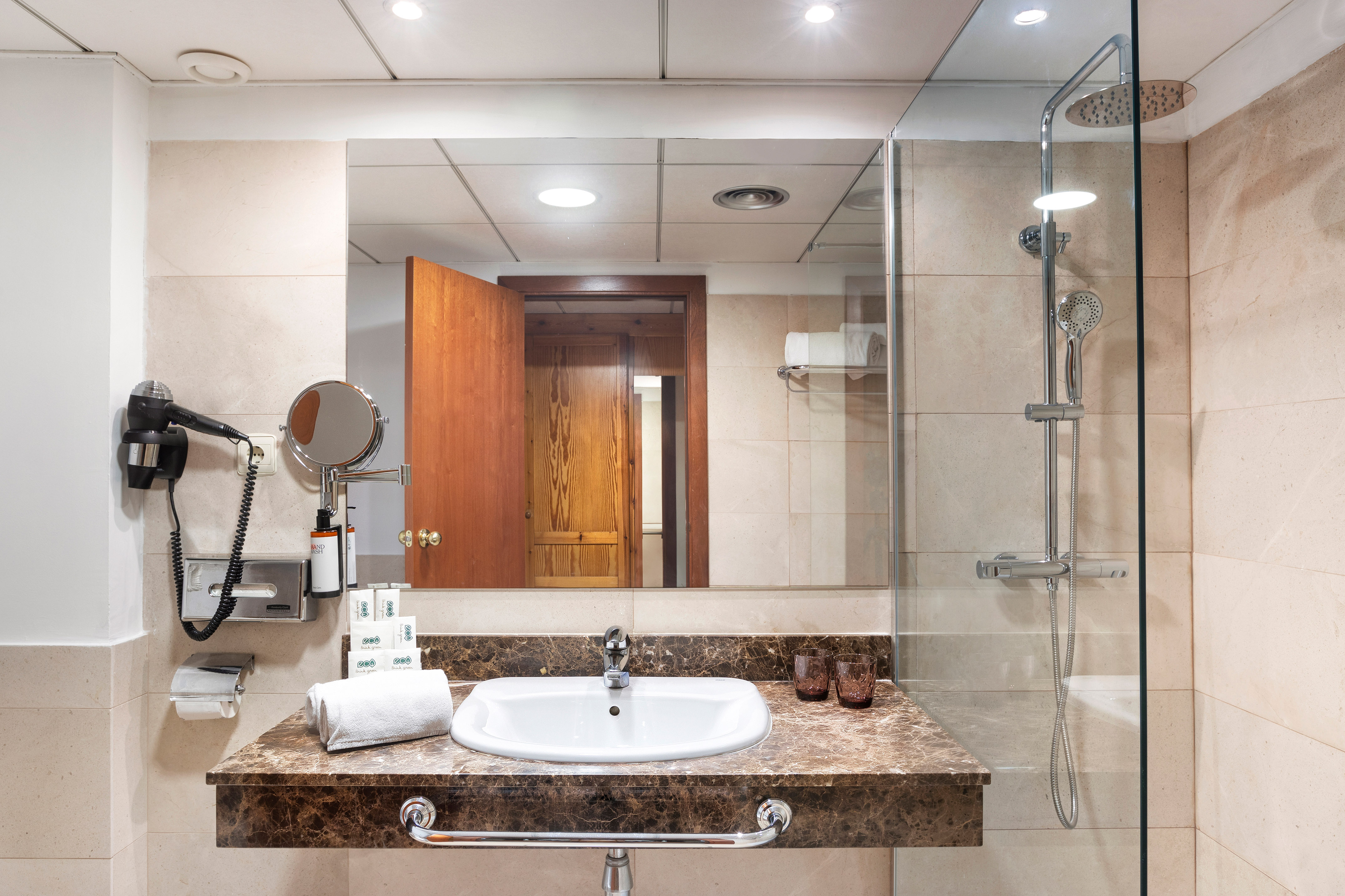 Hotel bathroom with marble vanity, white sink, large mirror, and glass shower.