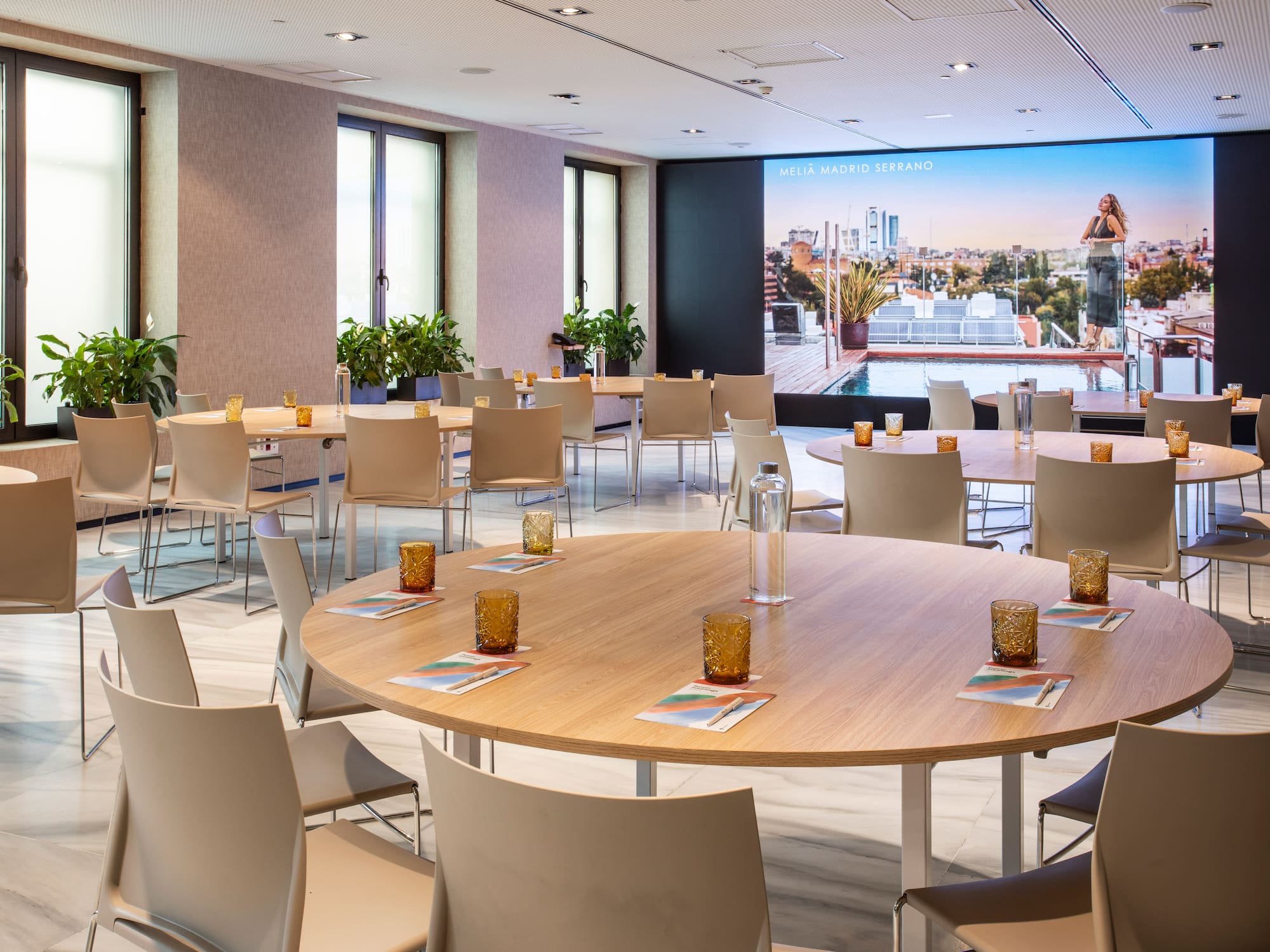 Conference room with round tables, chairs, and Meliá Madrid Serrano screen