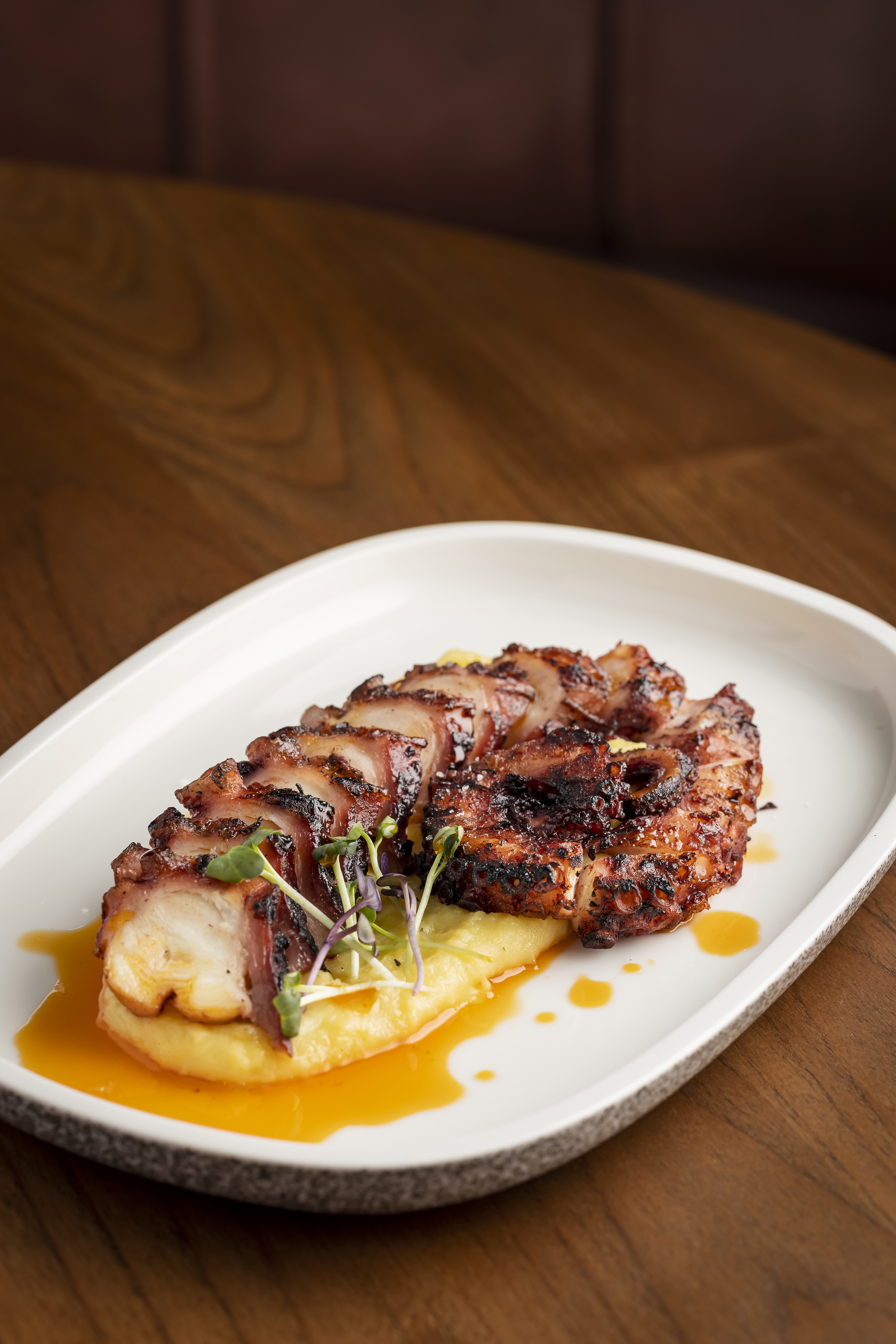 Grilled octopus on yellow purée with orange sauce and microgreens.