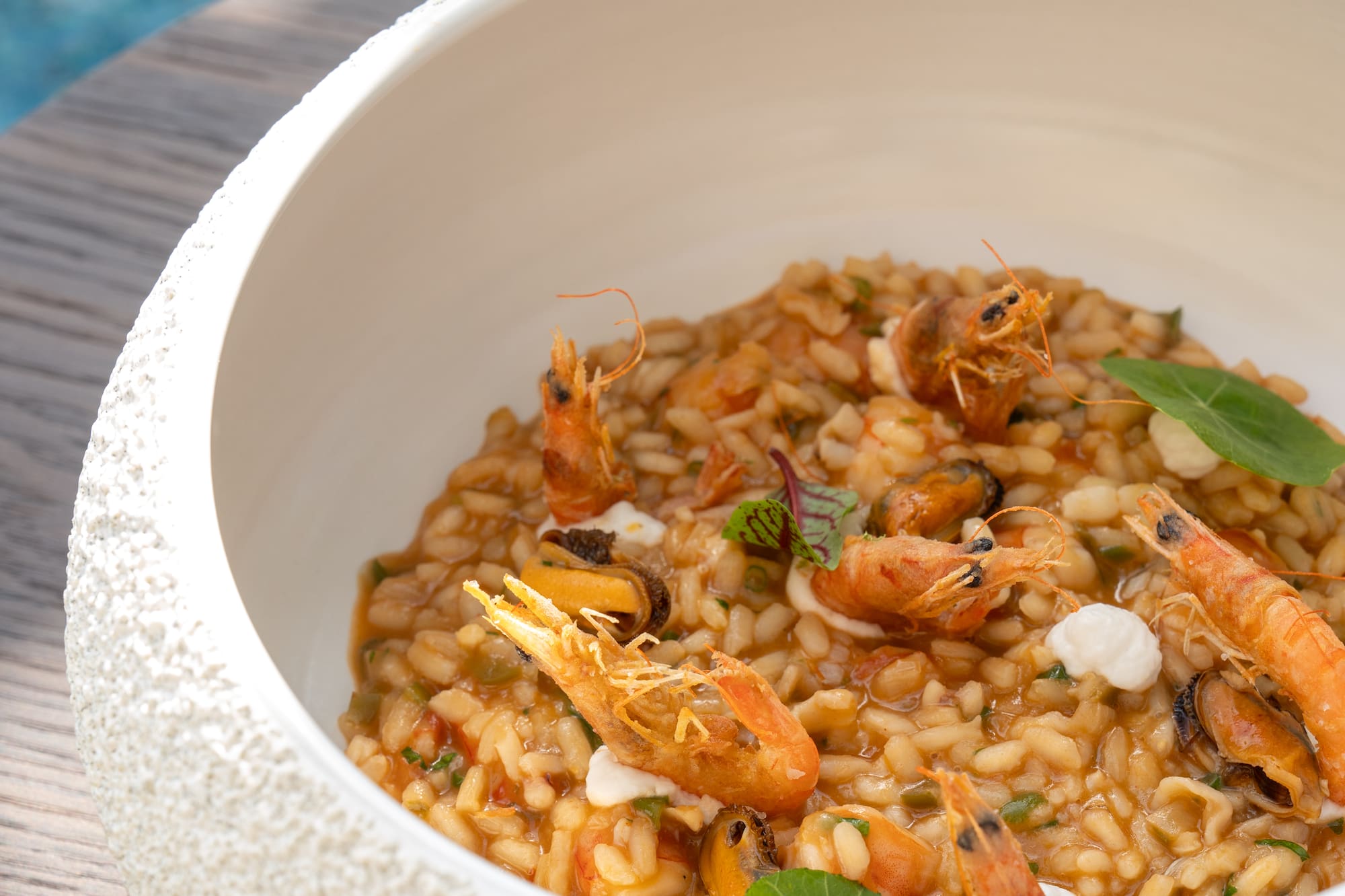 Risotto de mariscos con gambas y mejillones en cuenco, fondo de piscina azul.