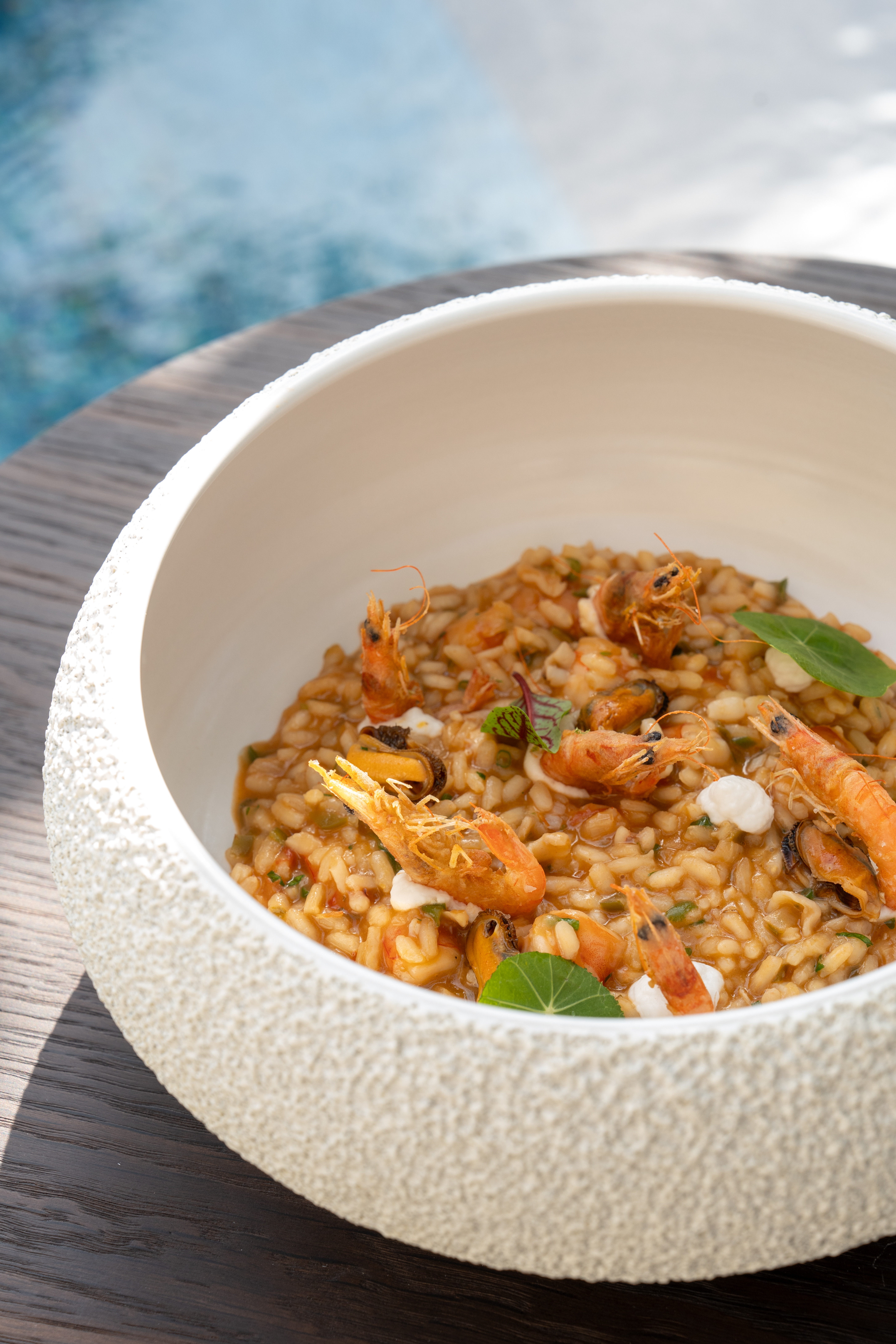 Risotto de mariscos con gambas y mejillones en cuenco, fondo de piscina azul.