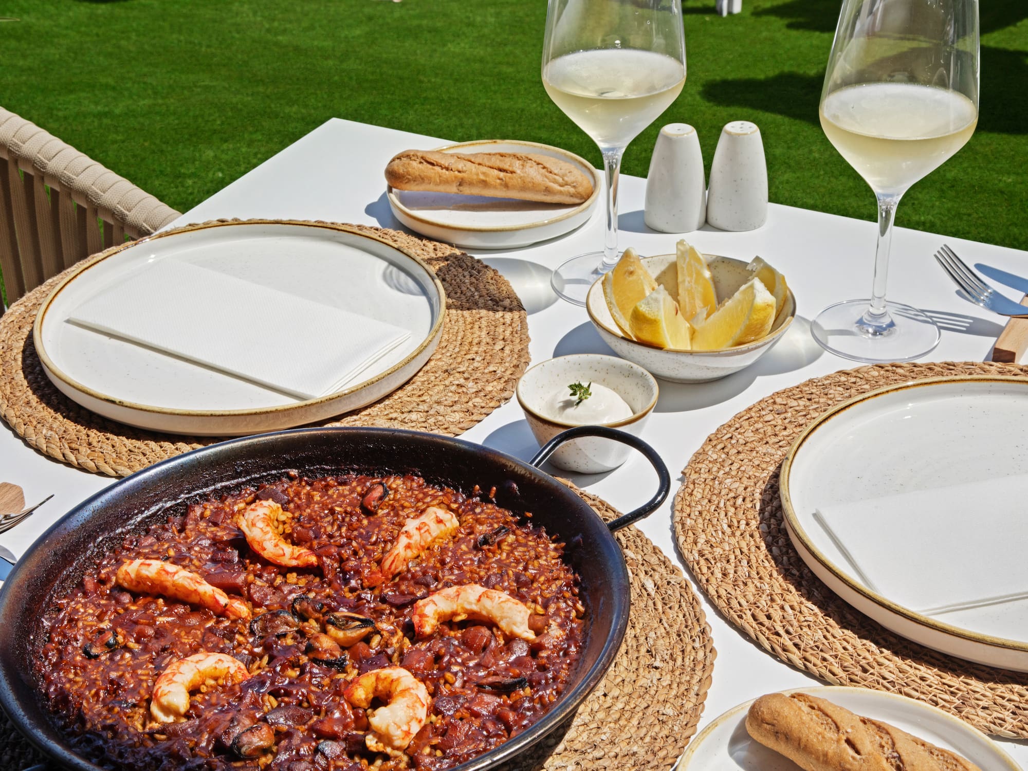 Paella de marisco con gambas y vino blanco en mesa exterior soleada.
