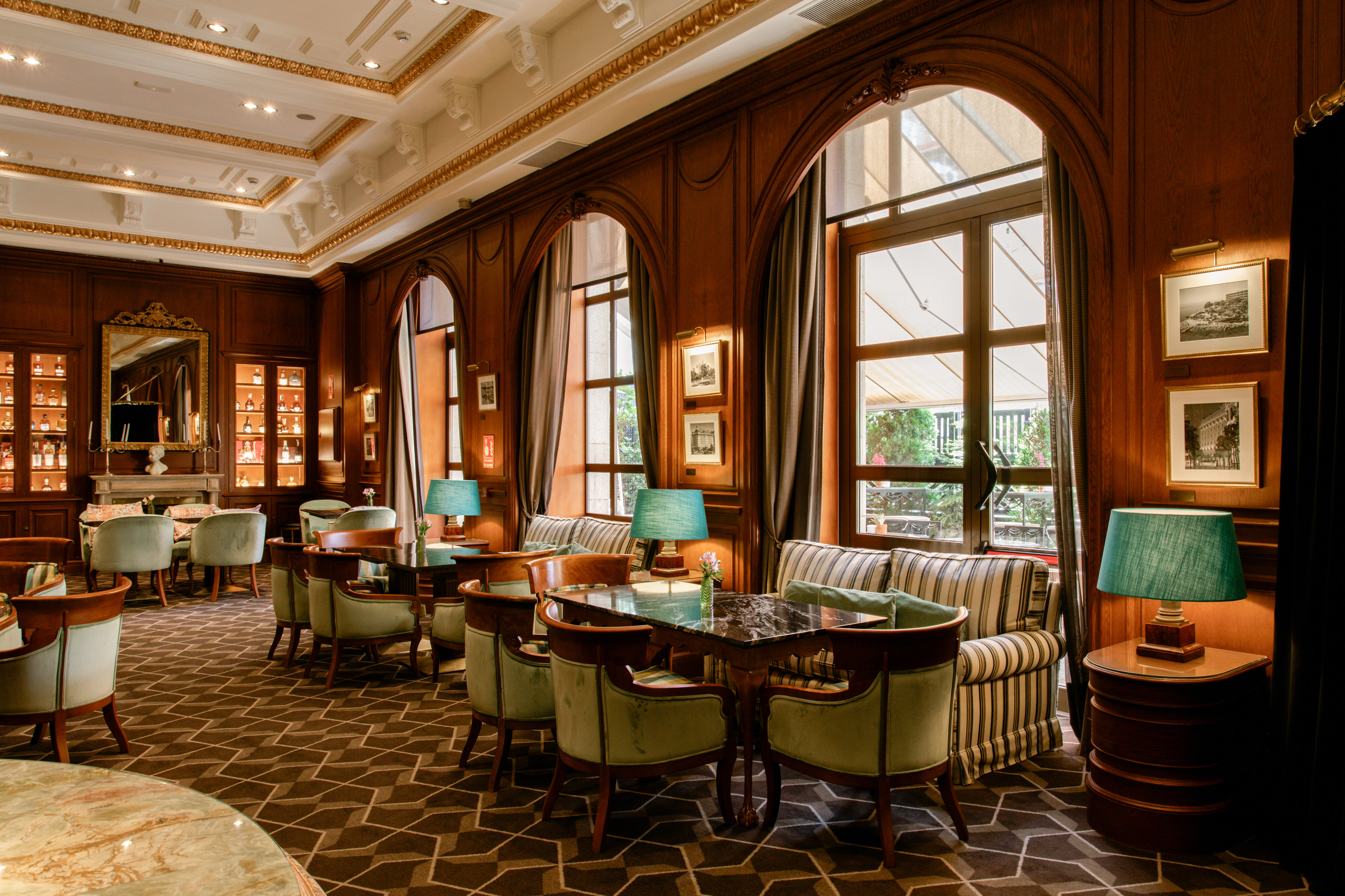Elegant hotel lounge with wood-paneled walls, arched windows, and plush seating.