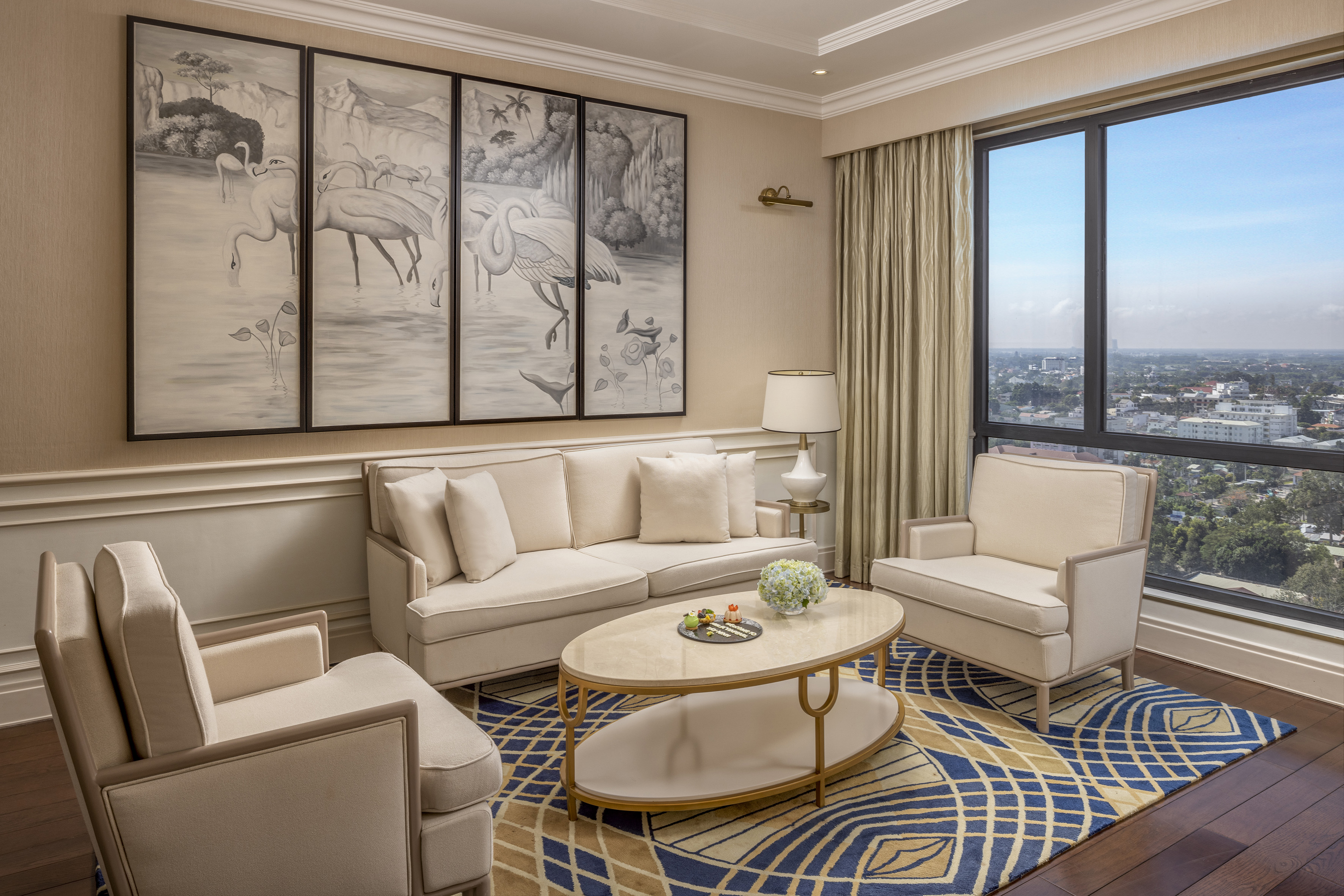 Luxury hotel suite lounge with city view, cream sofa, and flamingo mural.