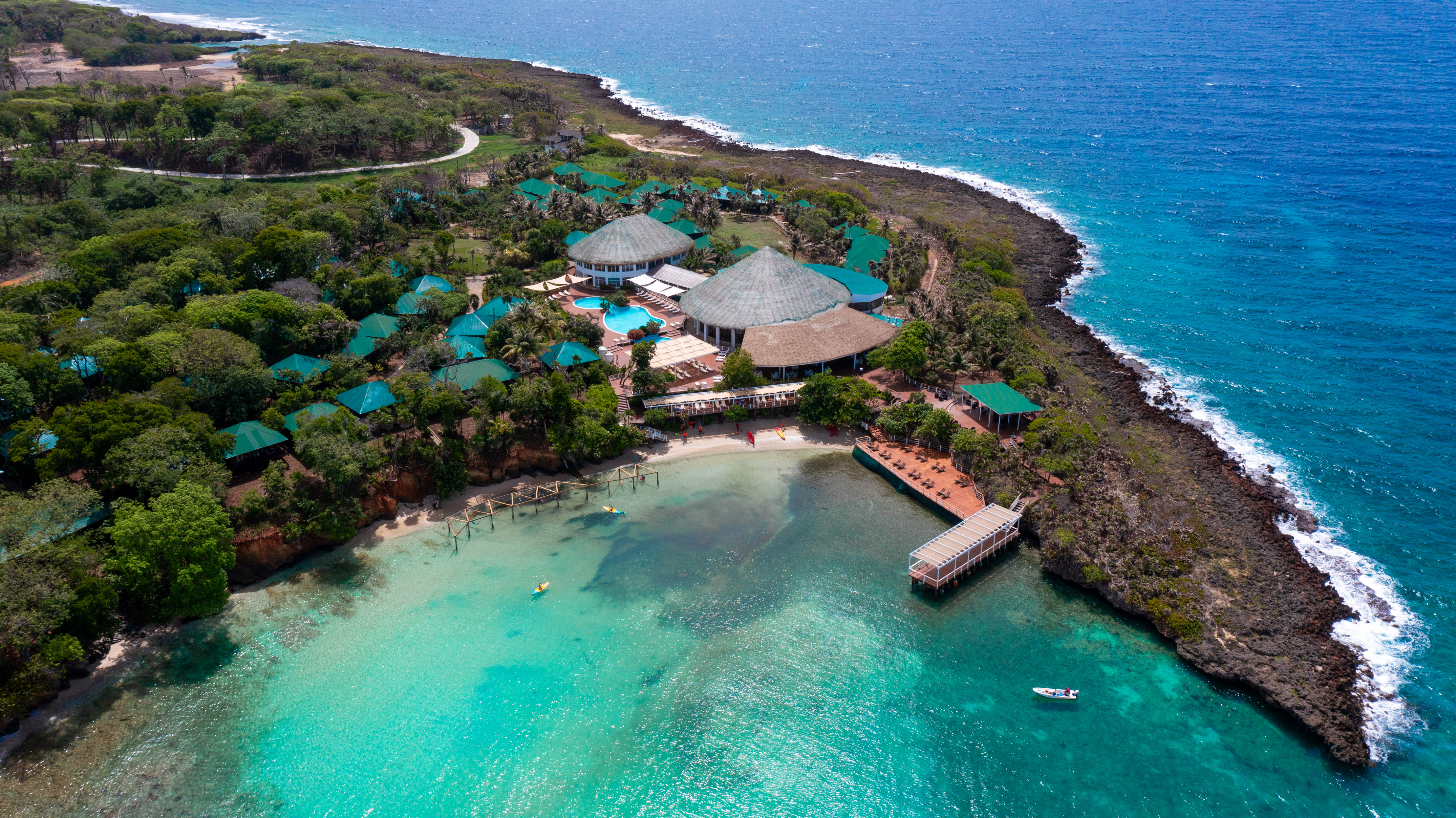 Tropical resort with green bungalows, clear turquoise ocean, beach, pier.