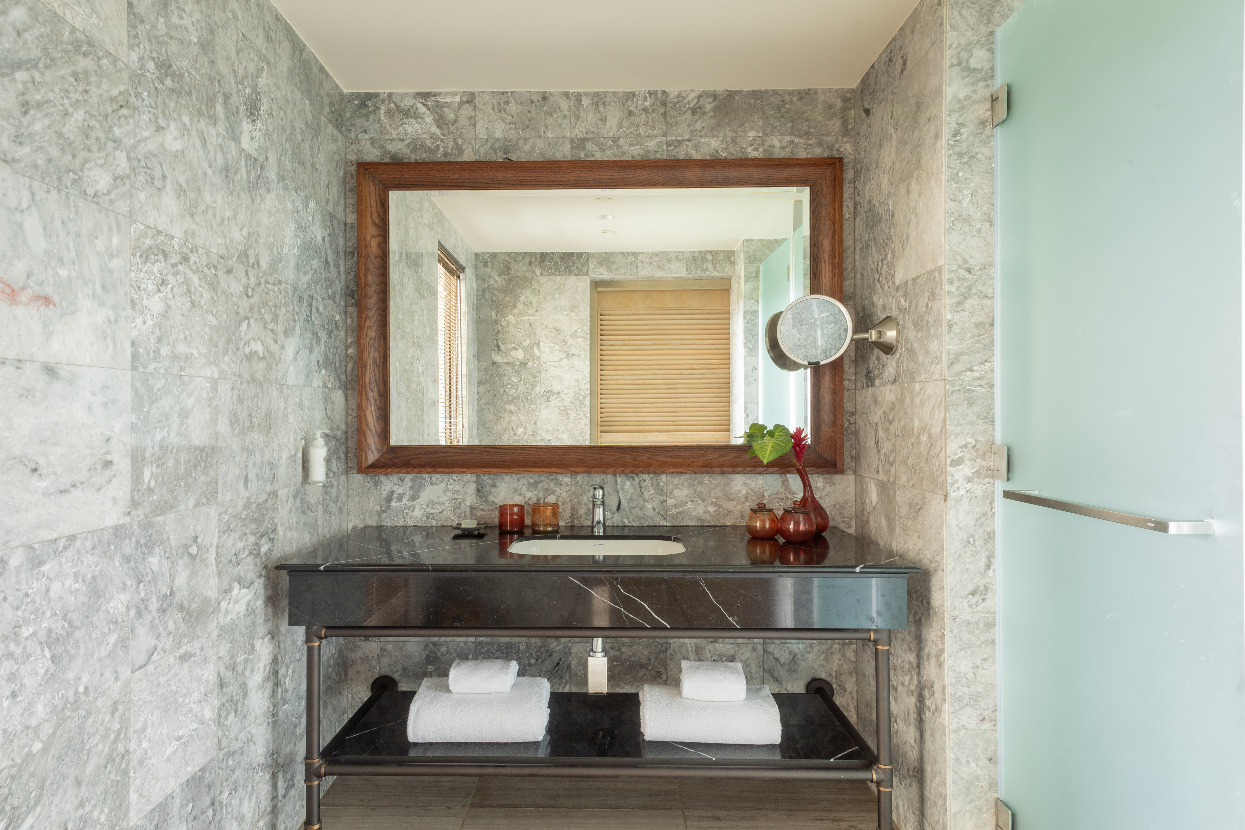 Bathroom vanity with black marble counter, large wooden mirror, and grey tiled walls.