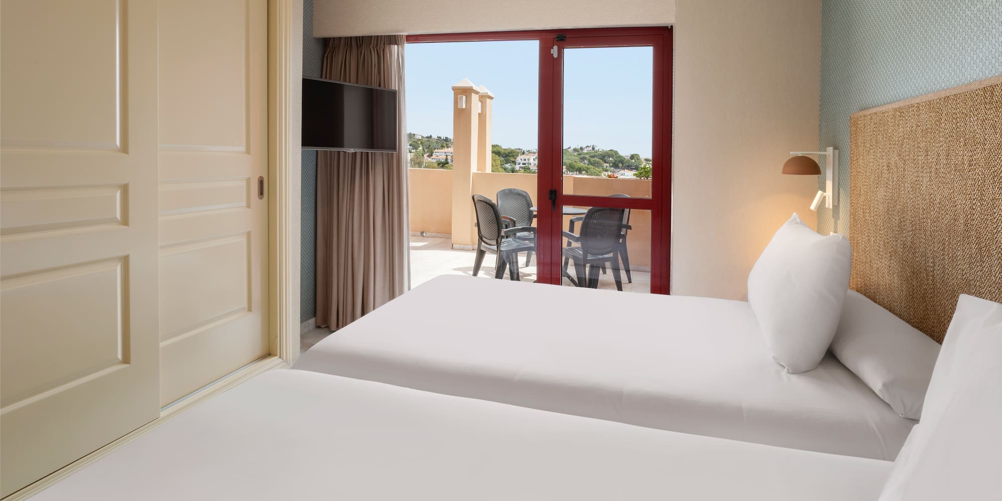 Resort twin bedroom with balcony, outdoor chairs, and woven headboard.