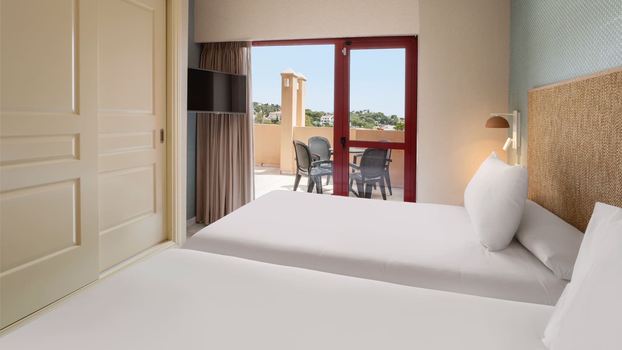 Bright twin hotel room with private balcony, outdoor furniture, and sunny view.