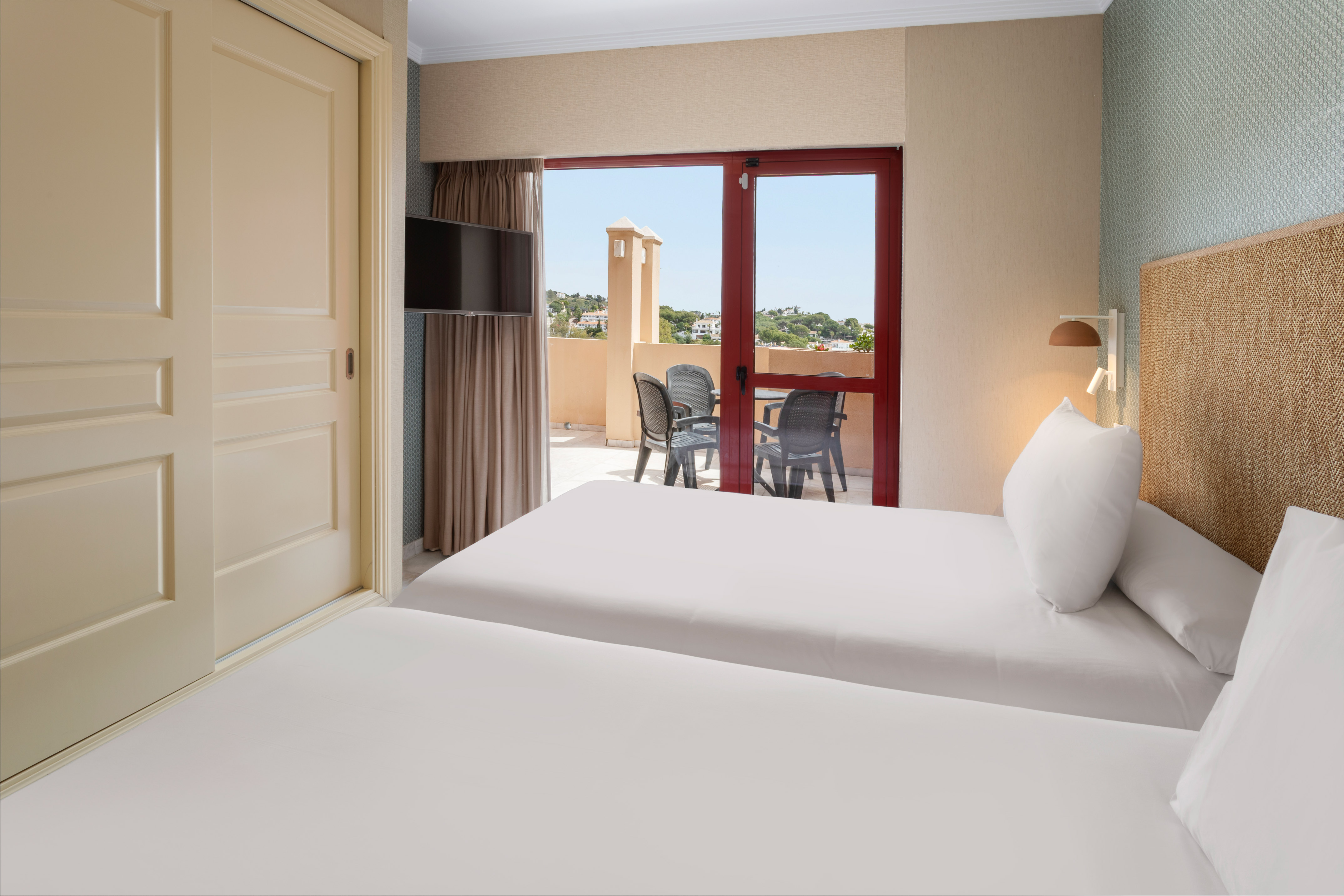 Bright twin hotel room with private balcony, outdoor furniture, and sunny view.