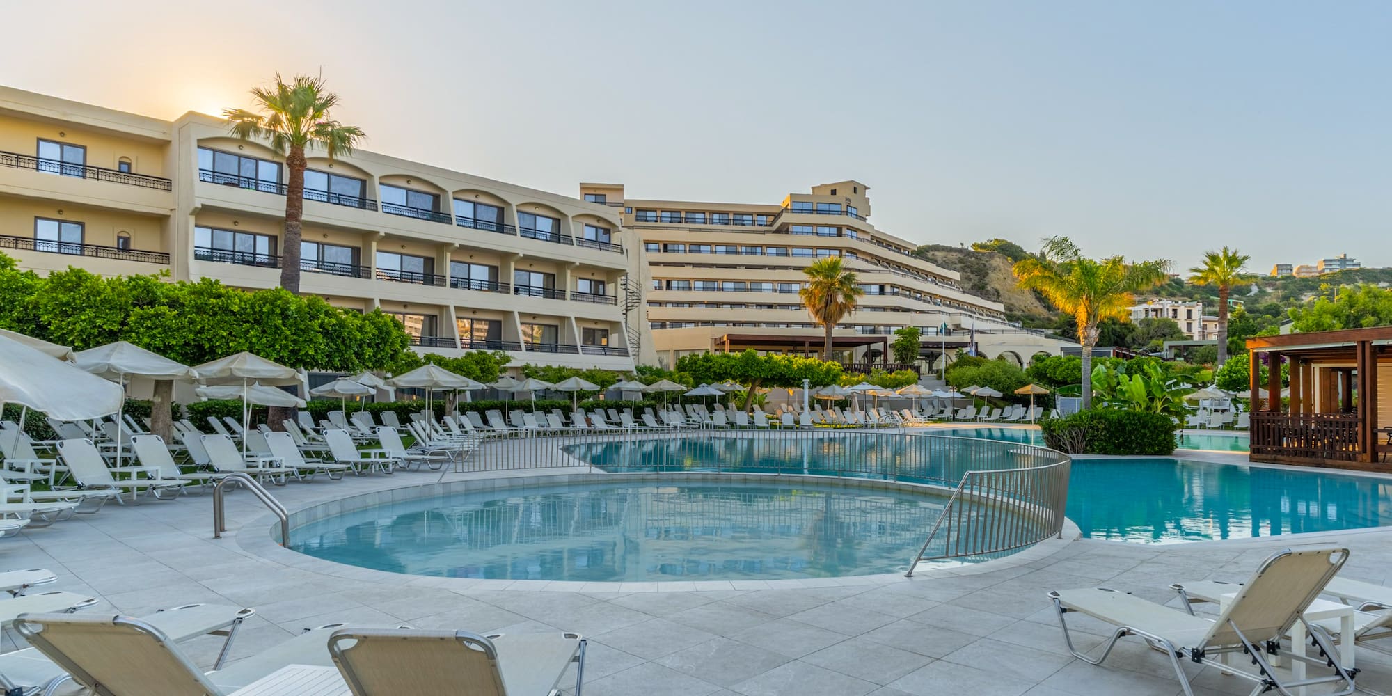 Hotel resort with swimming pools, lounge chairs, and palm trees at sunrise.