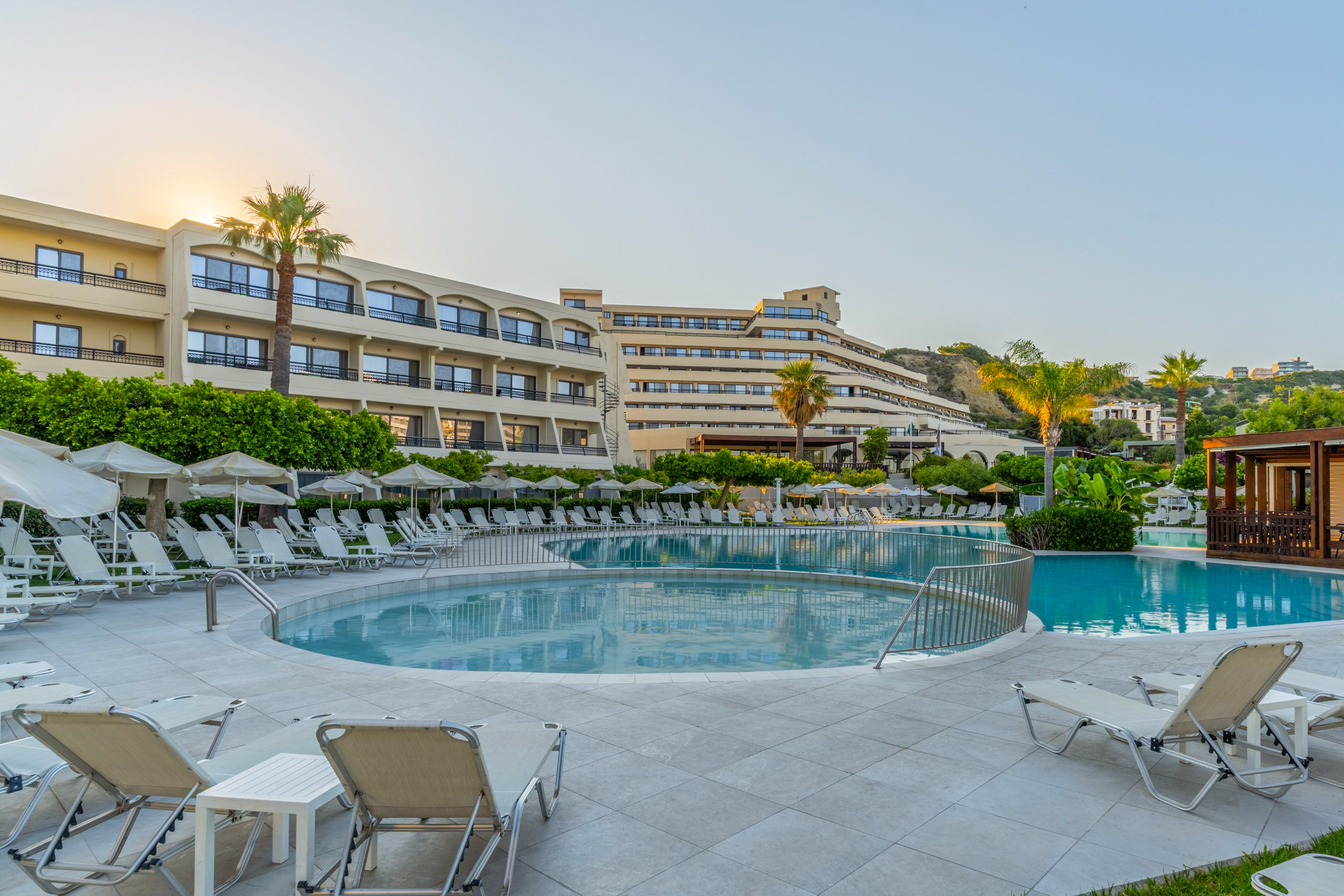 Hotel resort with swimming pools, lounge chairs, and palm trees at sunrise.