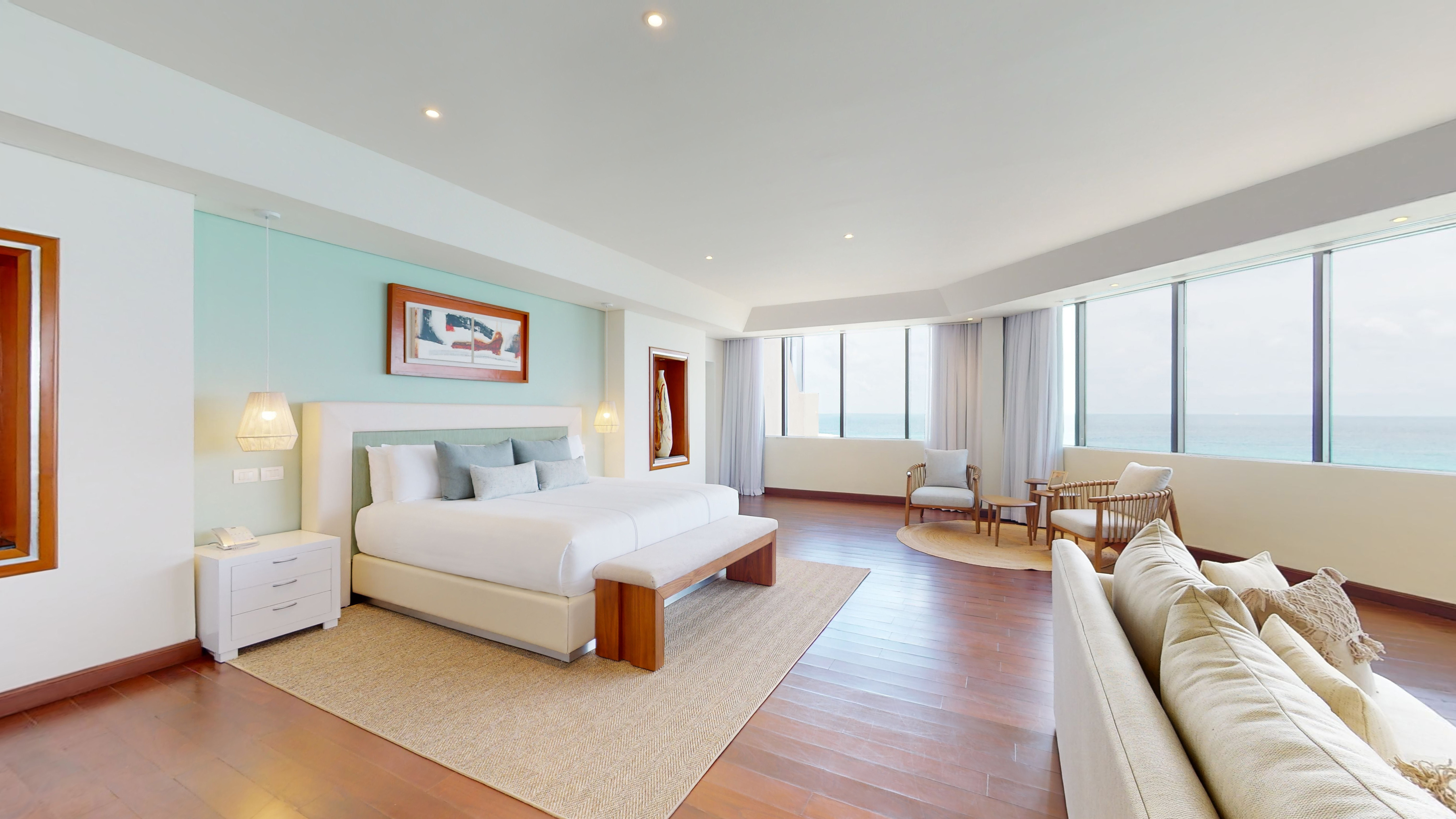 Spacious ocean view hotel suite with large bed and floor-to-ceiling windows.