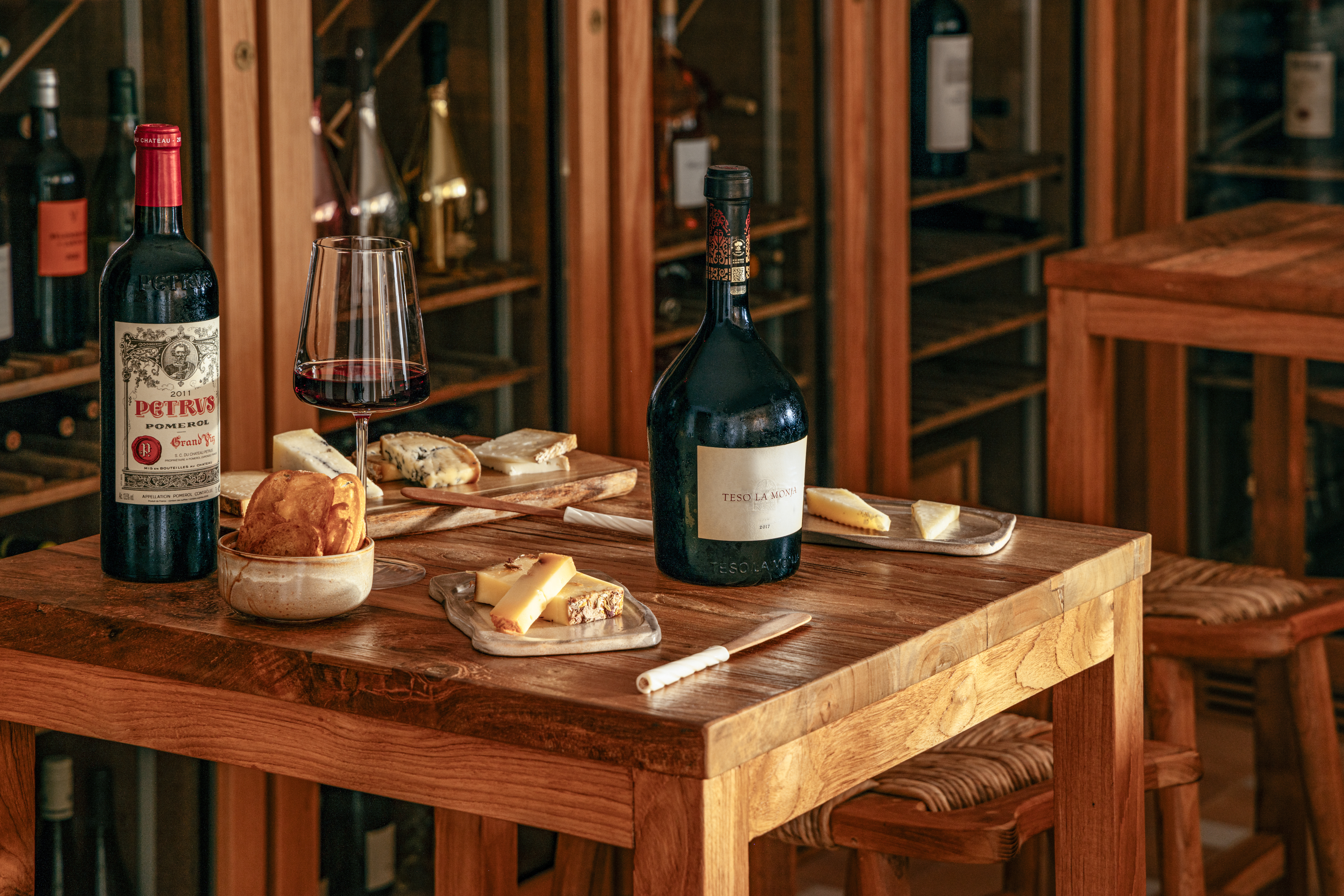 Red wine tasting: Petrus, Teso La Monja, cheese, bread on cellar table.