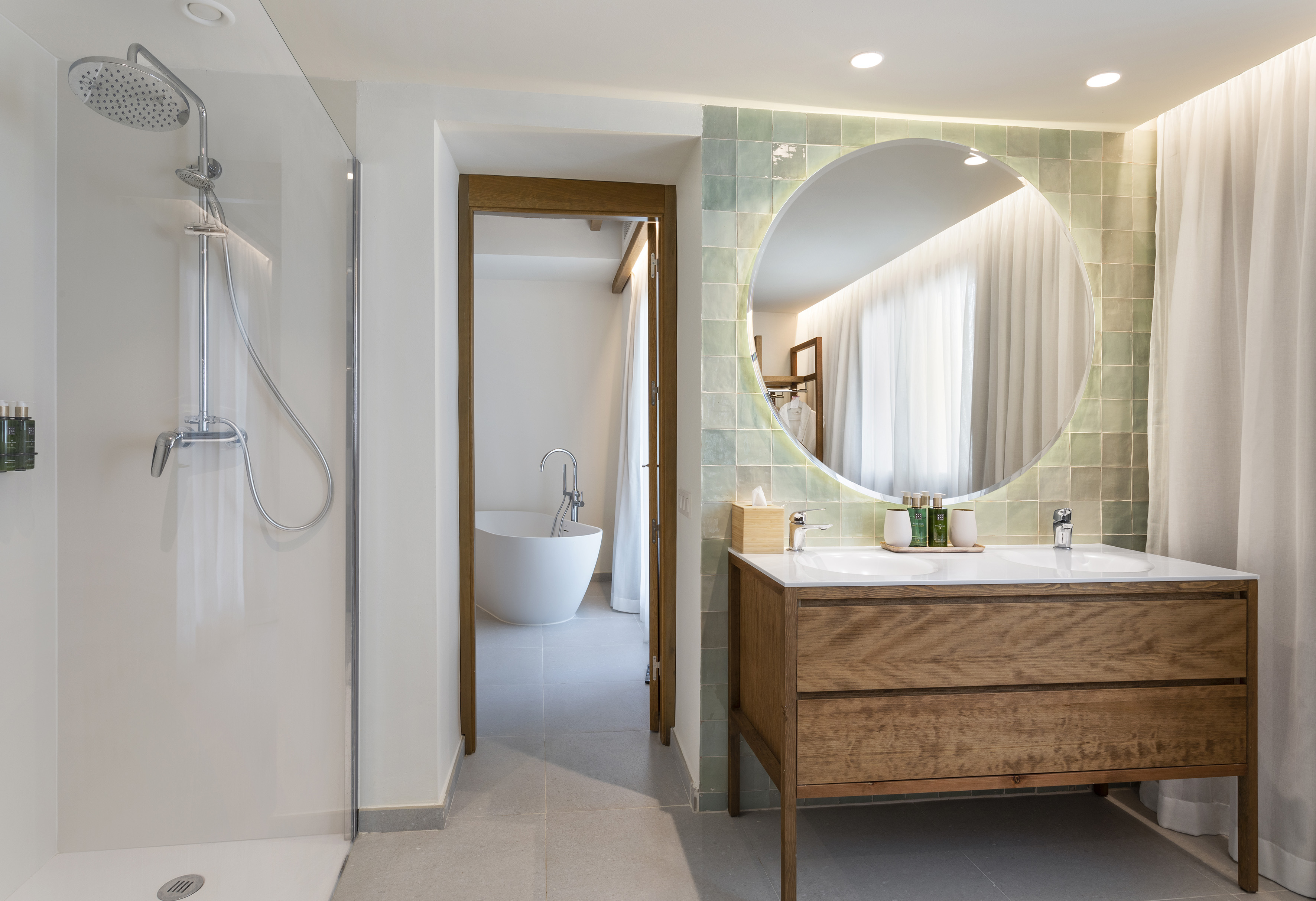 Modern bathroom with shower, wood vanity, round mirror, green tiles, and tub.