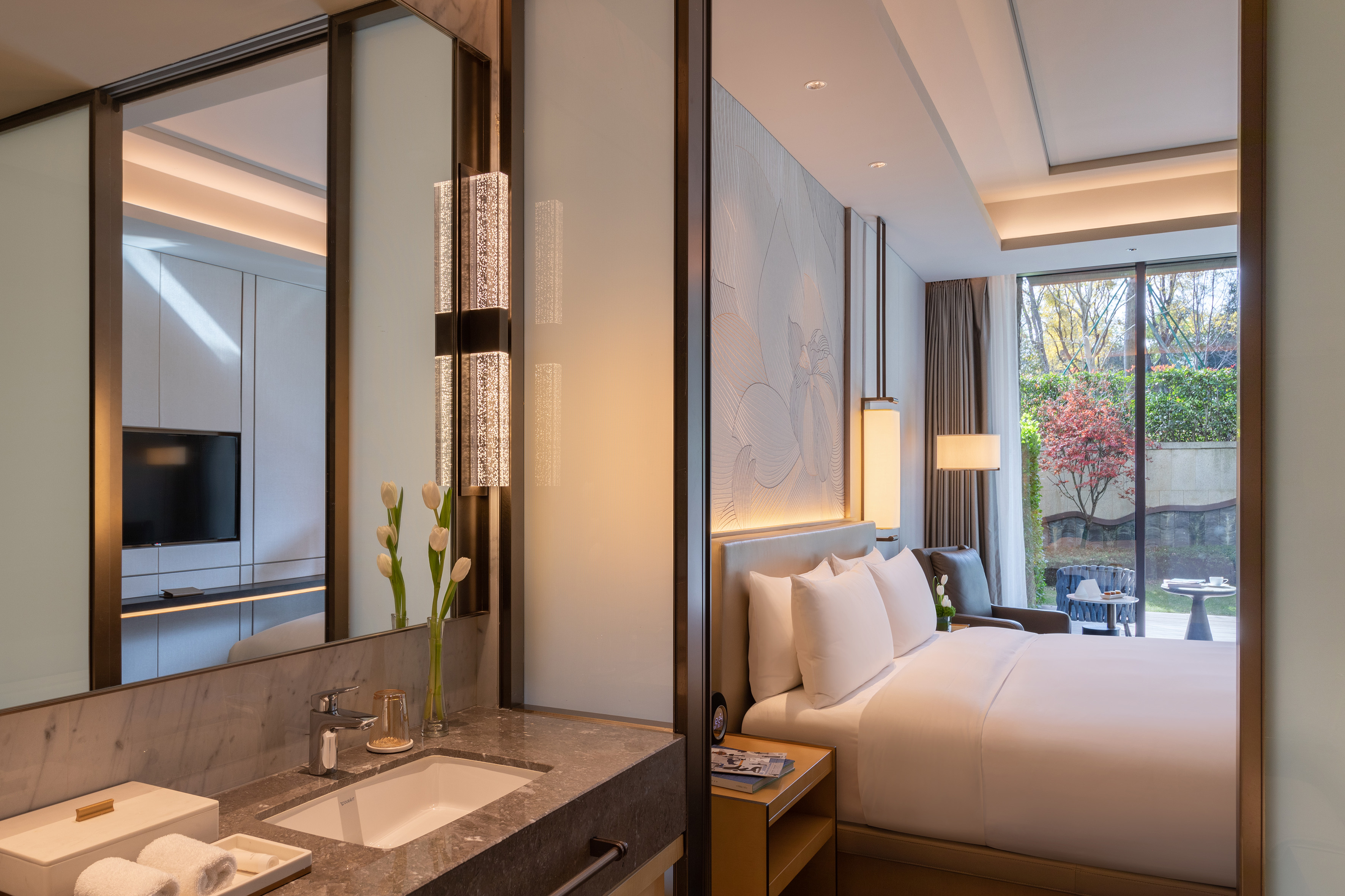 Modern luxury hotel suite with garden view, bedroom, and elegant bathroom vanity.