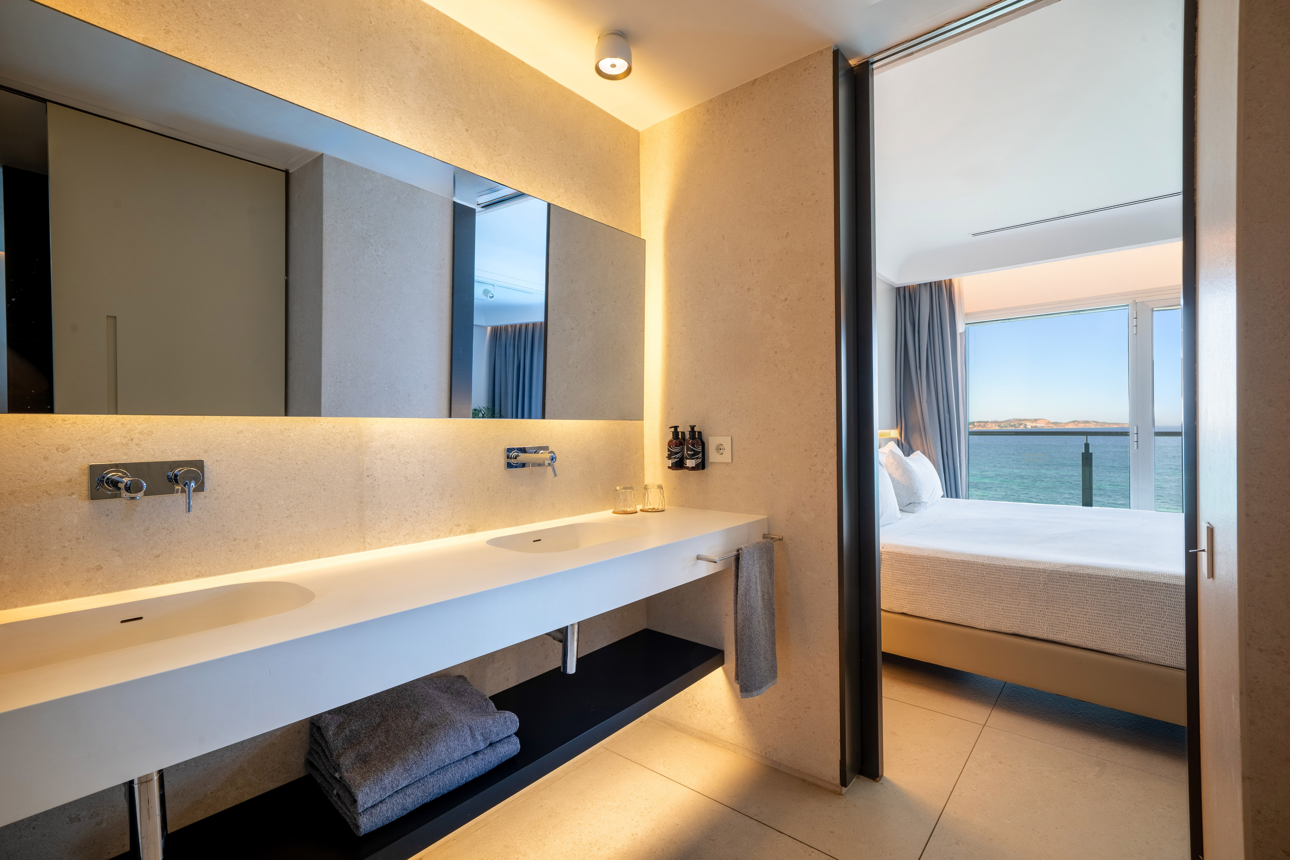 Luxury hotel bathroom with double vanity and ocean view bedroom suite.